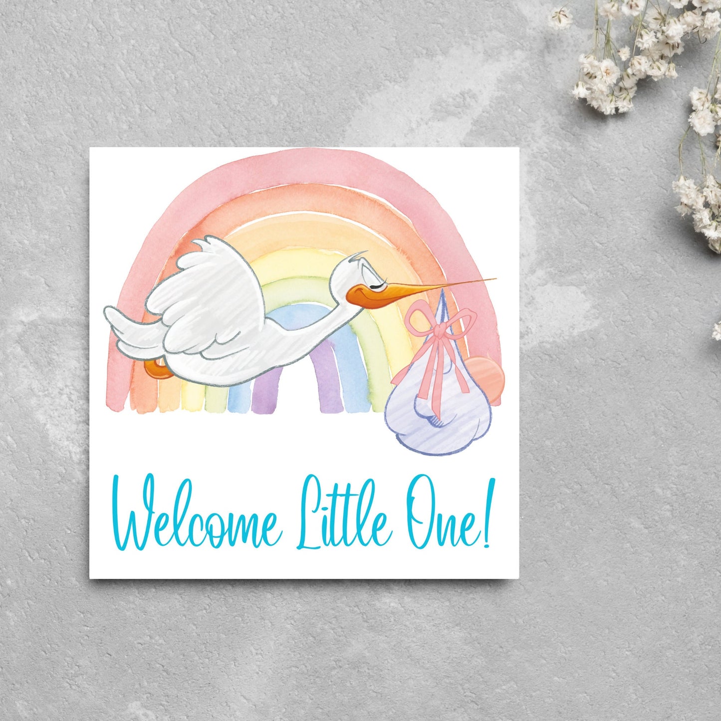 square new baby card with a flying cartoon stork delivering a swaddled baby against a watercolour rainbow in pastel shades. A cursive style text reads 'welcome little one' in a light blue font at the bottom of the card
