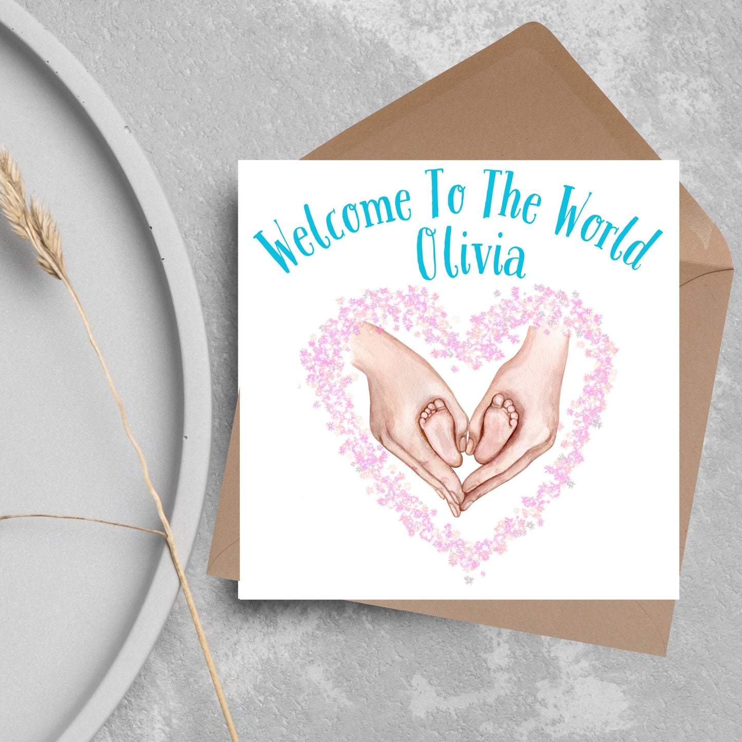 image of a square card with an illustration of hands holding newborn feet in a heart shape surrounded by pink flowers. Above the image is blue text that reads 'welcome to the world olivia' in a handwritten style font