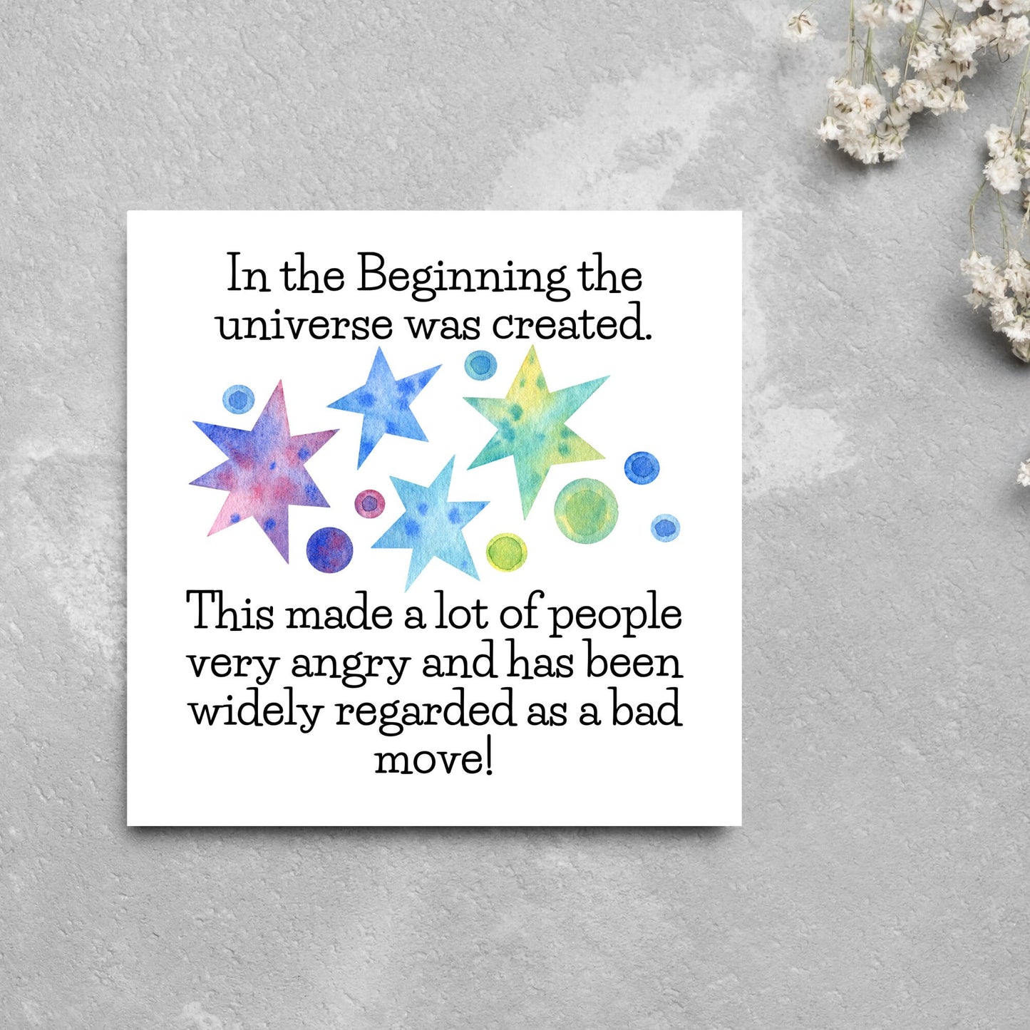 square card with watercolour abstract stars and planets and the text - in the beginning the universe was created. This made a lot of people very angry and has been widely regarded as a bad move! from the hitchhikers guide to the galaxy
