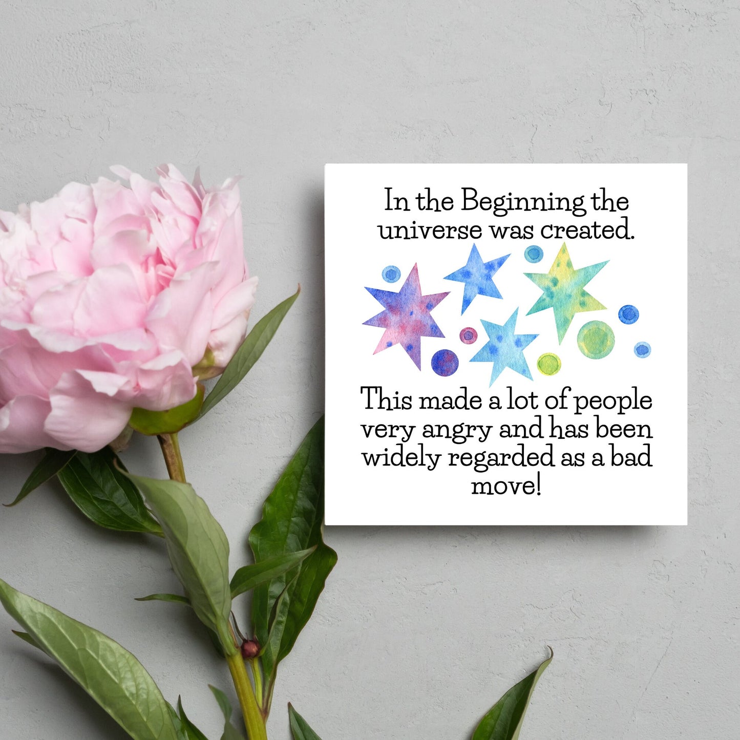 square card with watercolour abstract stars and planets and the text - in the beginning the universe was created. This made a lot of people very angry and has been widely regarded as a bad move! from the hitchhikers guide to the galaxy