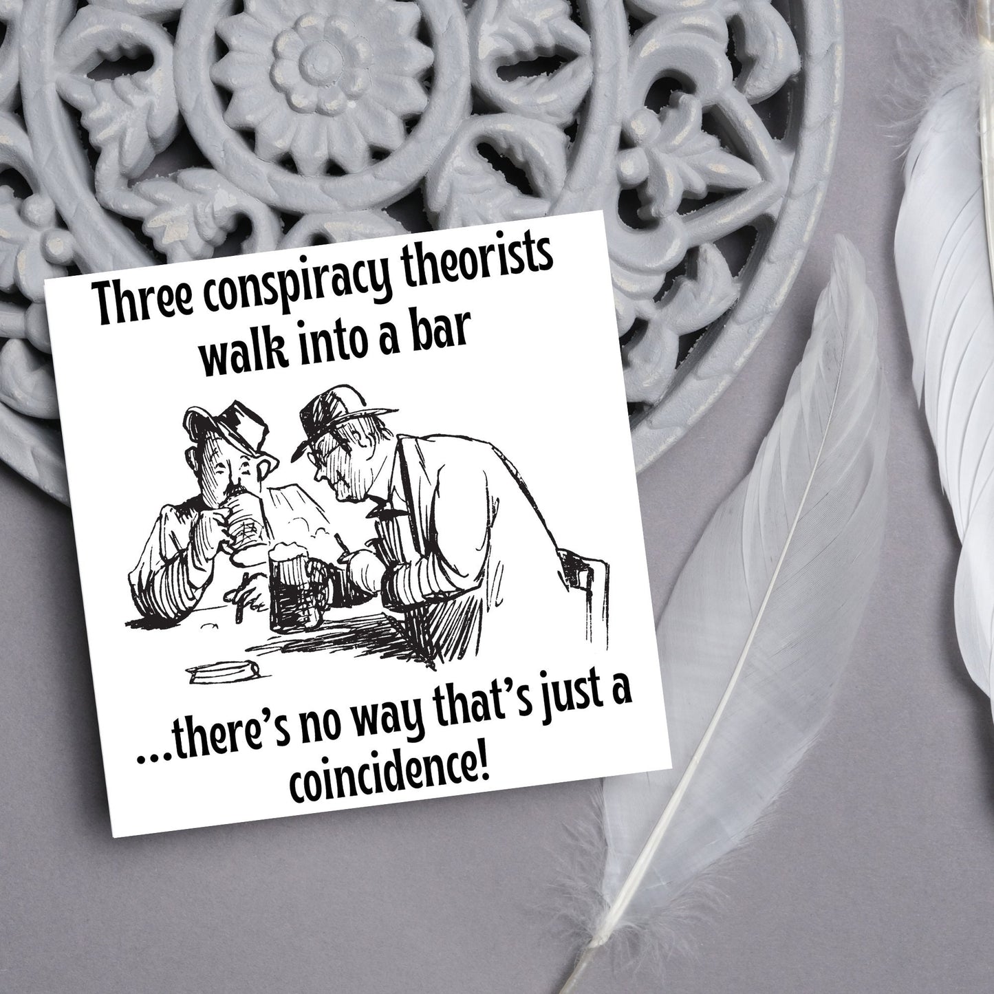 Image of a square greetings card with a hand drawn black and white line cartoon sketch of two old men at a bar drinking beer with the text- 3 conspiracy theorists walk into a bar....there's no way that's just a coincidence!