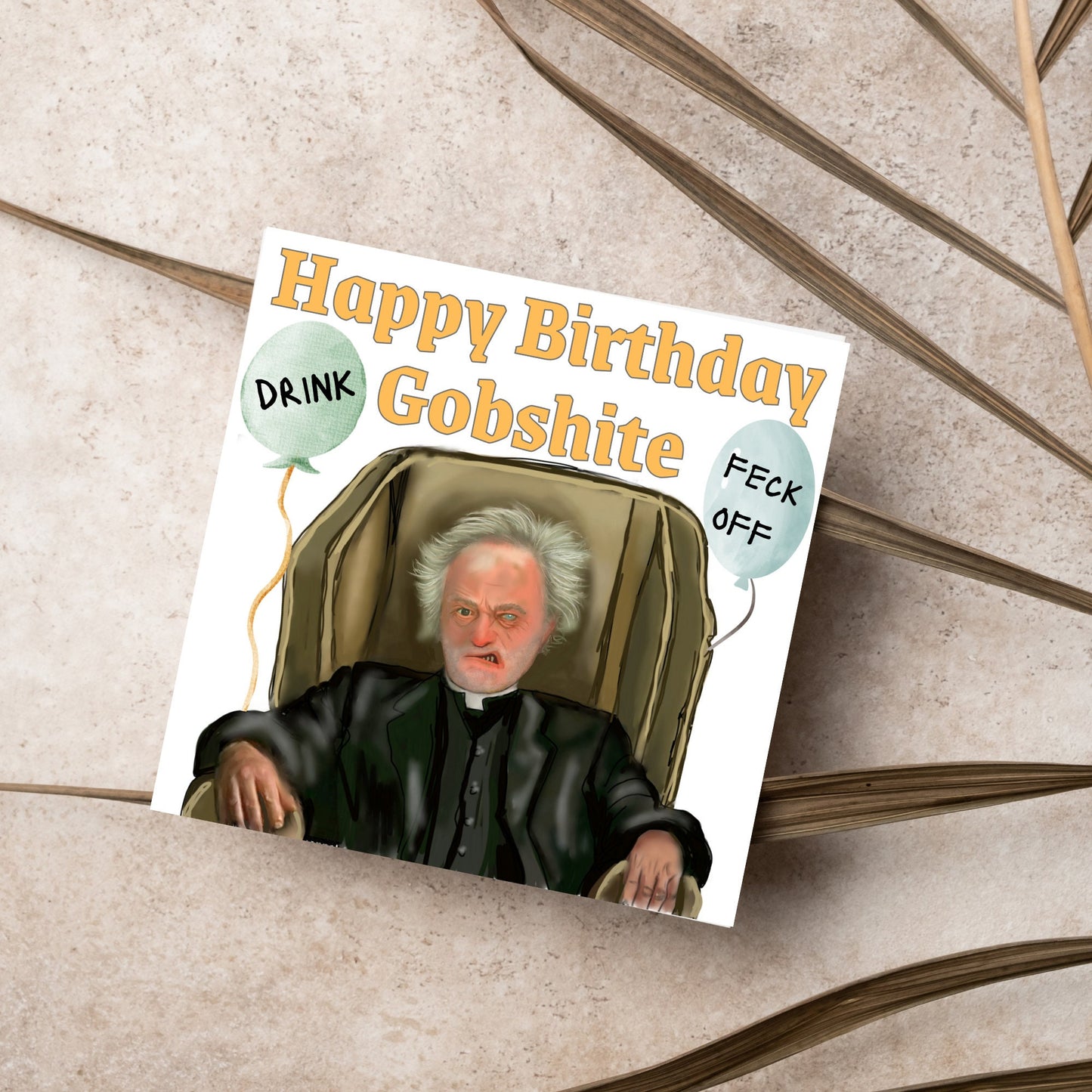 square birthday card with a hand drawn image of father jack from the tv show father ted. he is sitting in his chair looking mean with the text happy birthday gobshite above him. 2 balloons are next to him with feck off and drink on them