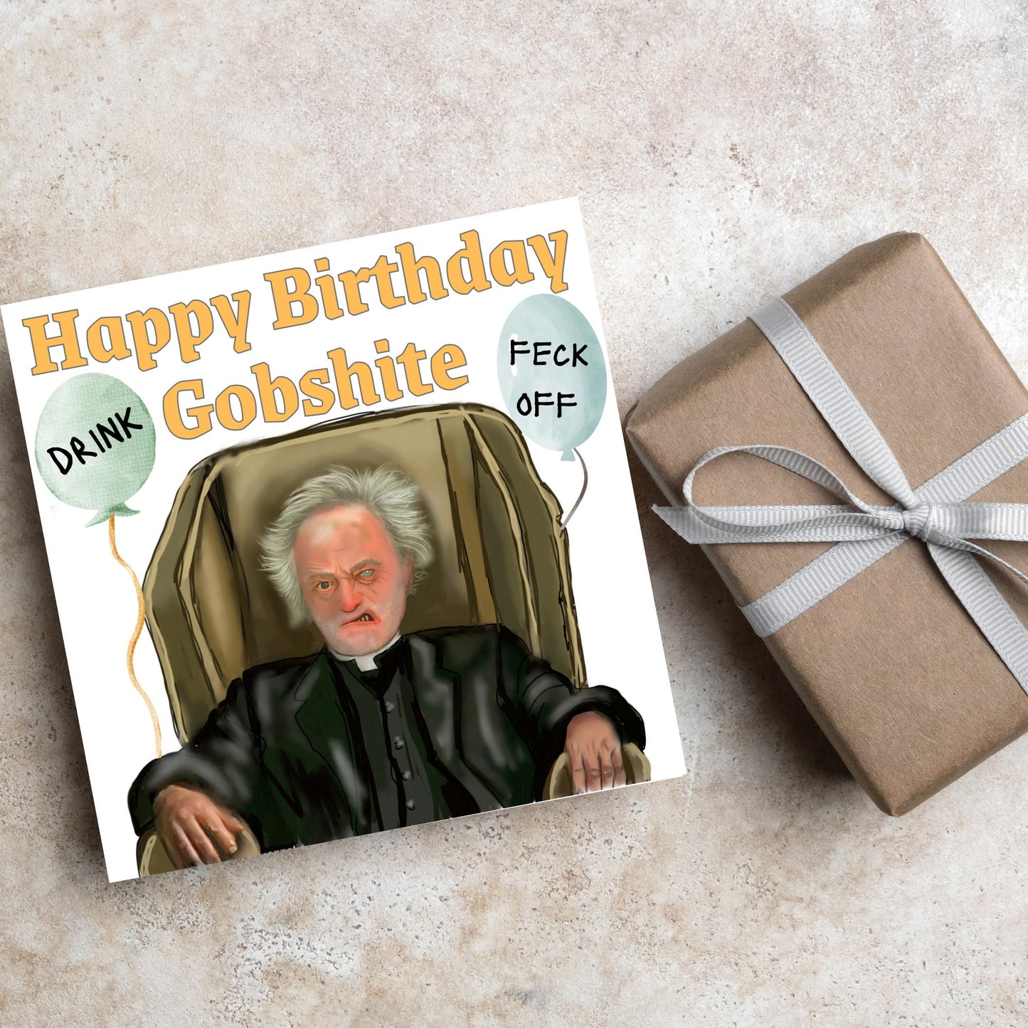 square birthday card with a hand drawn image of father jack from the tv show father ted. he is sitting in his chair looking mean with the text happy birthday gobshite above him. 2 balloons are next to him with feck off and drink on them