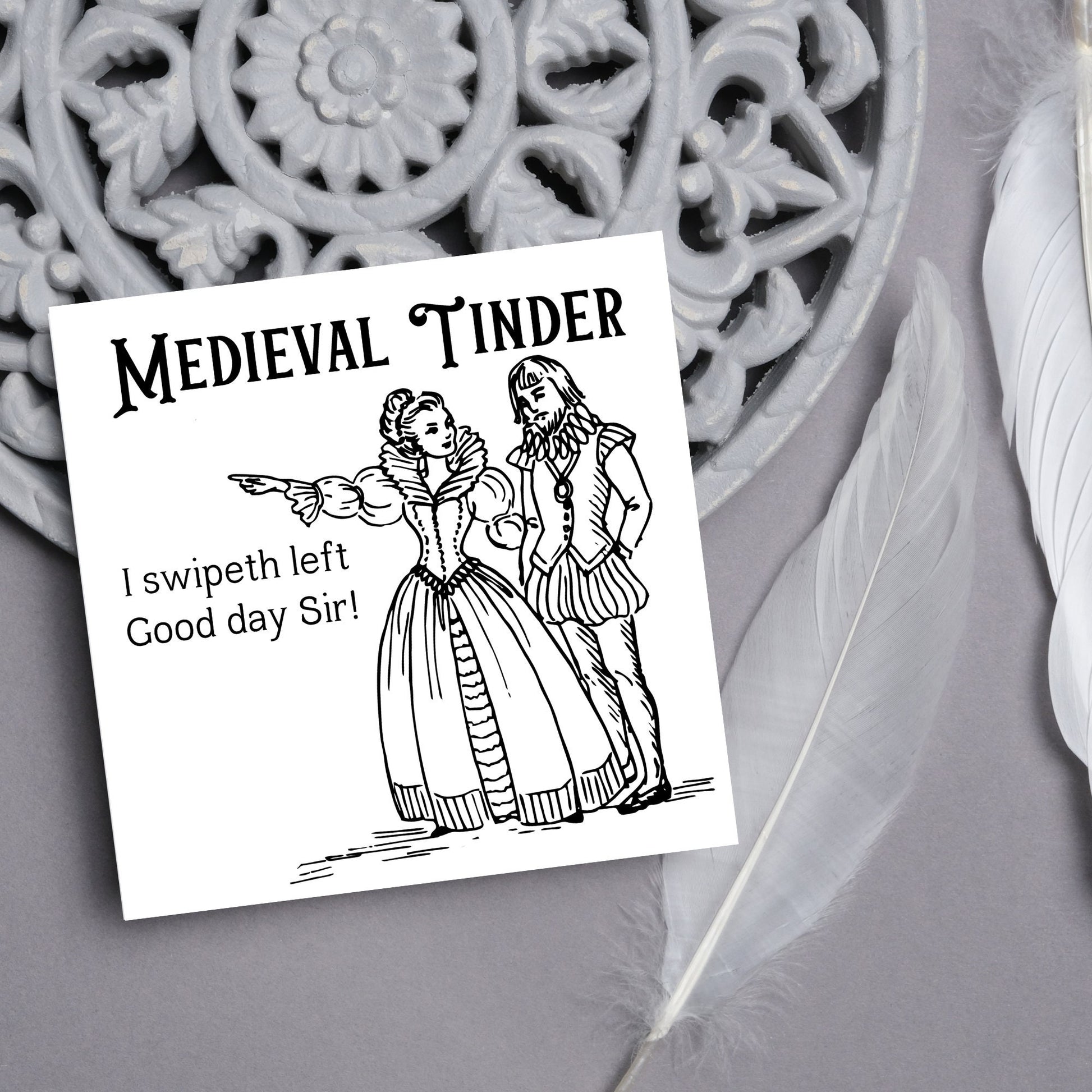 image of a square greetings card with a black and white hand drawn vintage style illustration of medieval man and woman, the woman pointing left and the text - medieval tinder. I swipeth left. Good day Sir! - in a vintage blackletter font