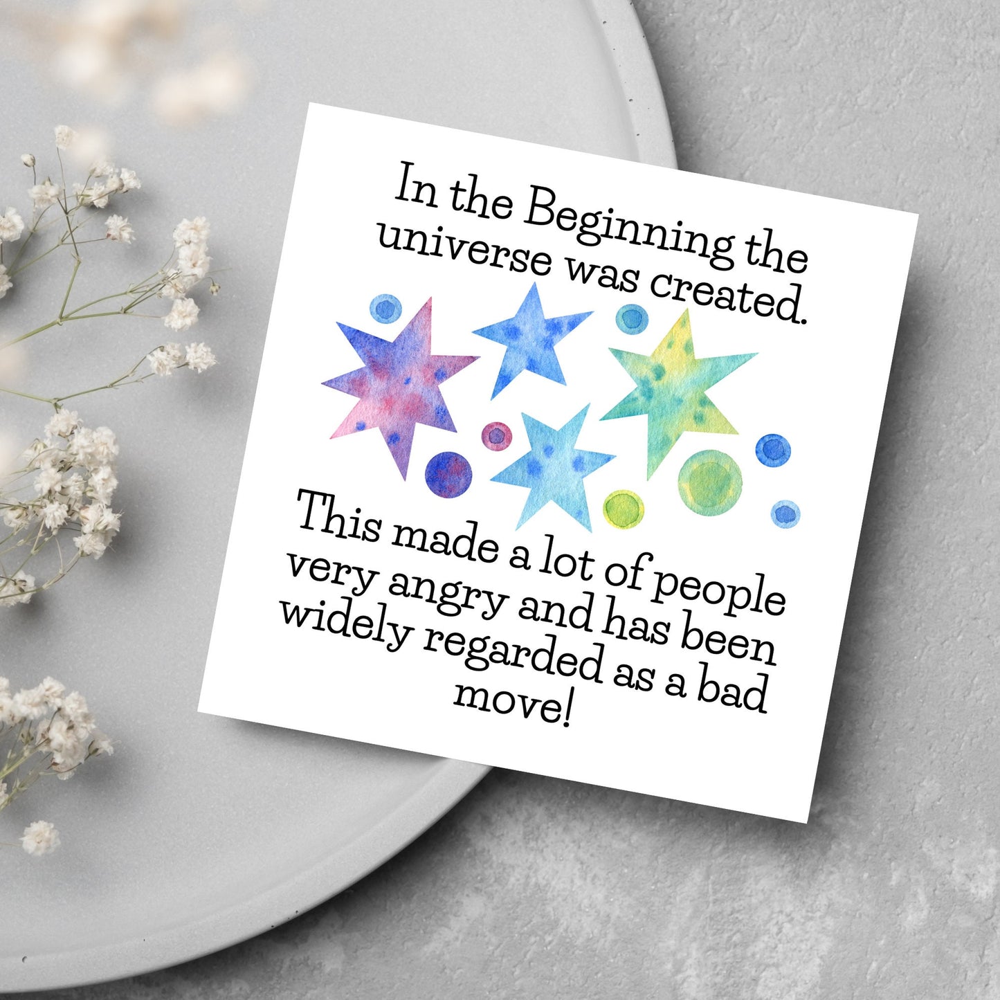 square card with watercolour abstract stars and planets and the text - in the beginning the universe was created. This made a lot of people very angry and has been widely regarded as a bad move! from the hitchhikers guide to the galaxy
