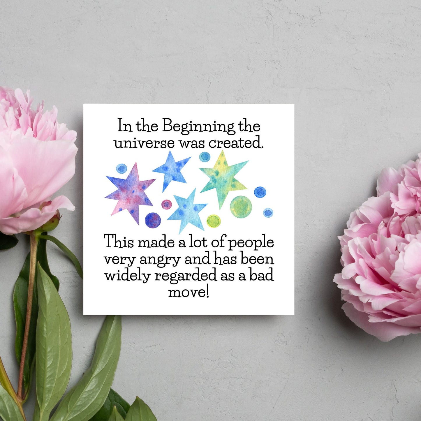 square card with watercolour abstract stars and planets and the text - in the beginning the universe was created. This made a lot of people very angry and has been widely regarded as a bad move! from the hitchhikers guide to the galaxy