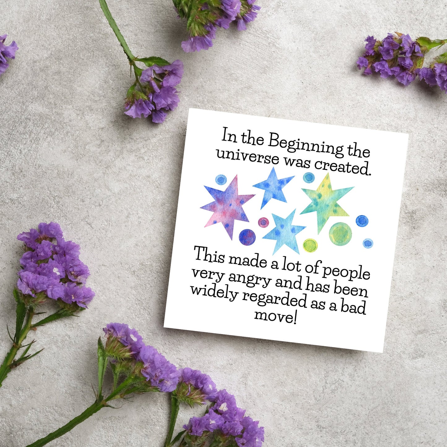 square card with watercolour abstract stars and planets and the text - in the beginning the universe was created. This made a lot of people very angry and has been widely regarded as a bad move! from the hitchhikers guide to the galaxy