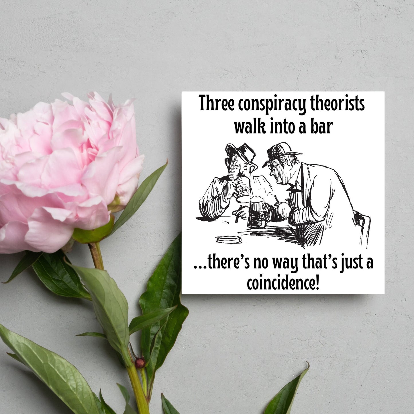 Image of a square greetings card with a hand drawn black and white line cartoon sketch of two old men at a bar drinking beer with the text- 3 conspiracy theorists walk into a bar....there's no way that's just a coincidence!