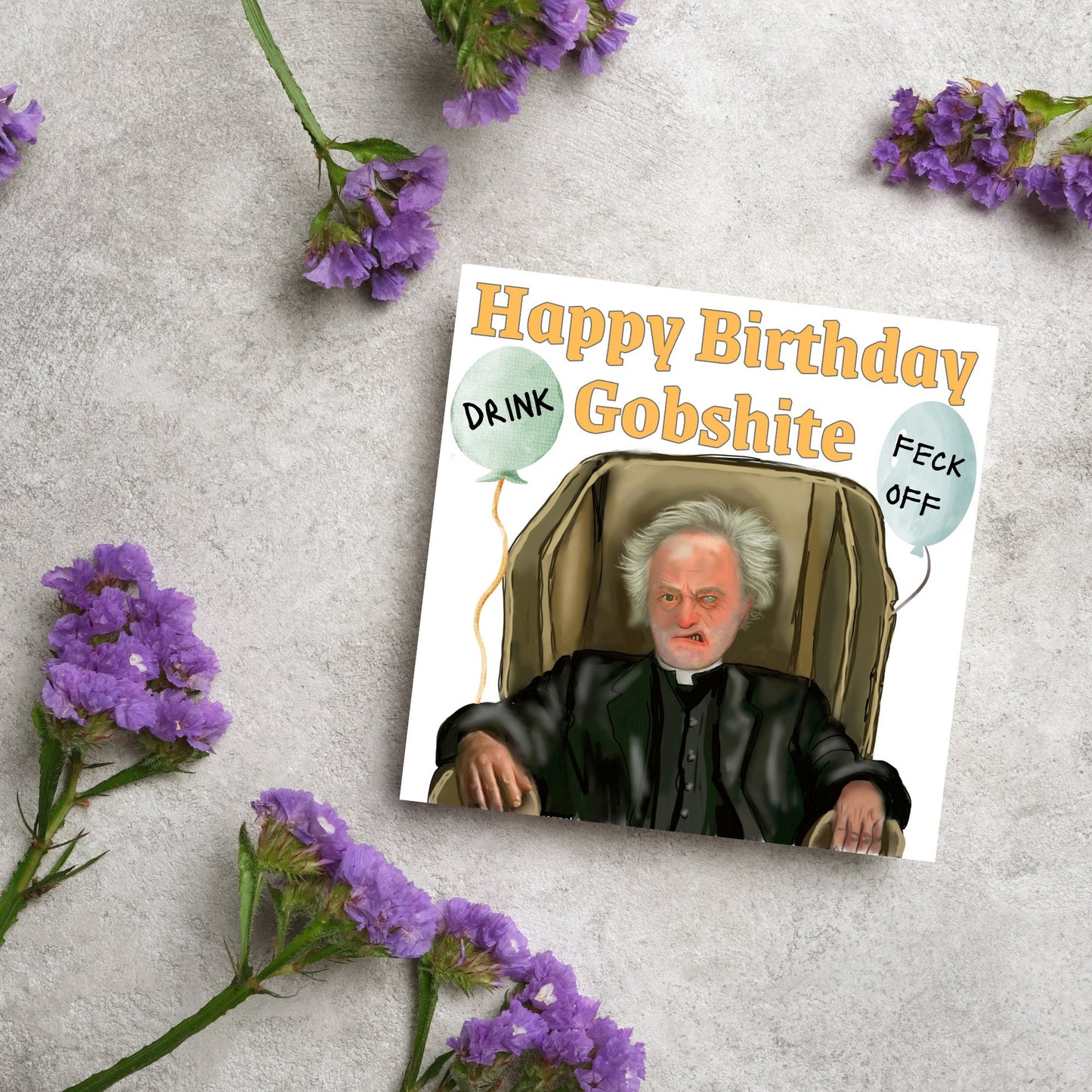 square birthday card with a hand drawn image of father jack from the tv show father ted. he is sitting in his chair looking mean with the text happy birthday gobshite above him. 2 balloons are next to him with feck off and drink on them