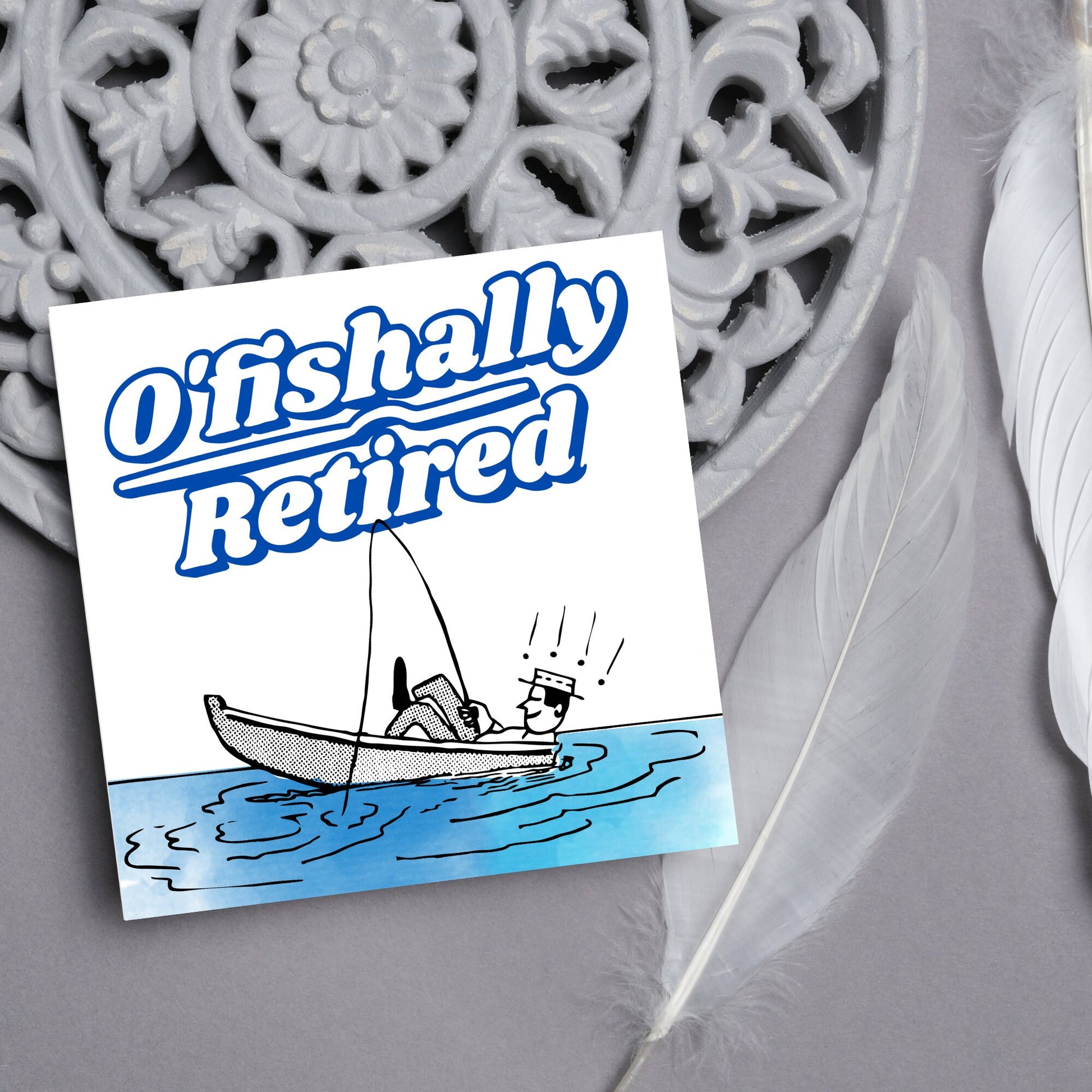 square card with a cartoon of a man in a boat looking happy and relaxed with a fishing rod. big blue and white text reads - ofishally retired'