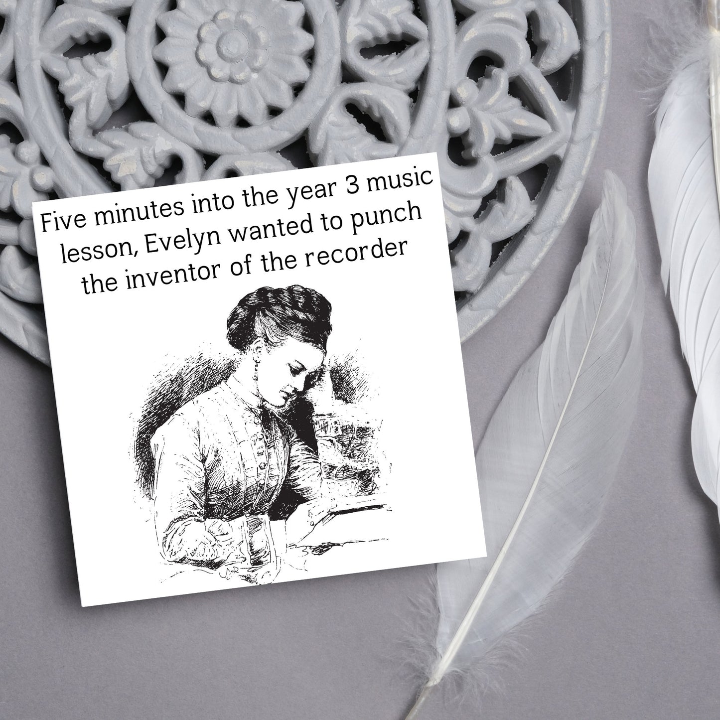 Image of a square greetings card with a black and white line drawing of a victorian lady sitting at a desk with her head in her hands and the text - five minutes into the tear 3 music lesson, evelyn wanted to punch the inventor of the recorder