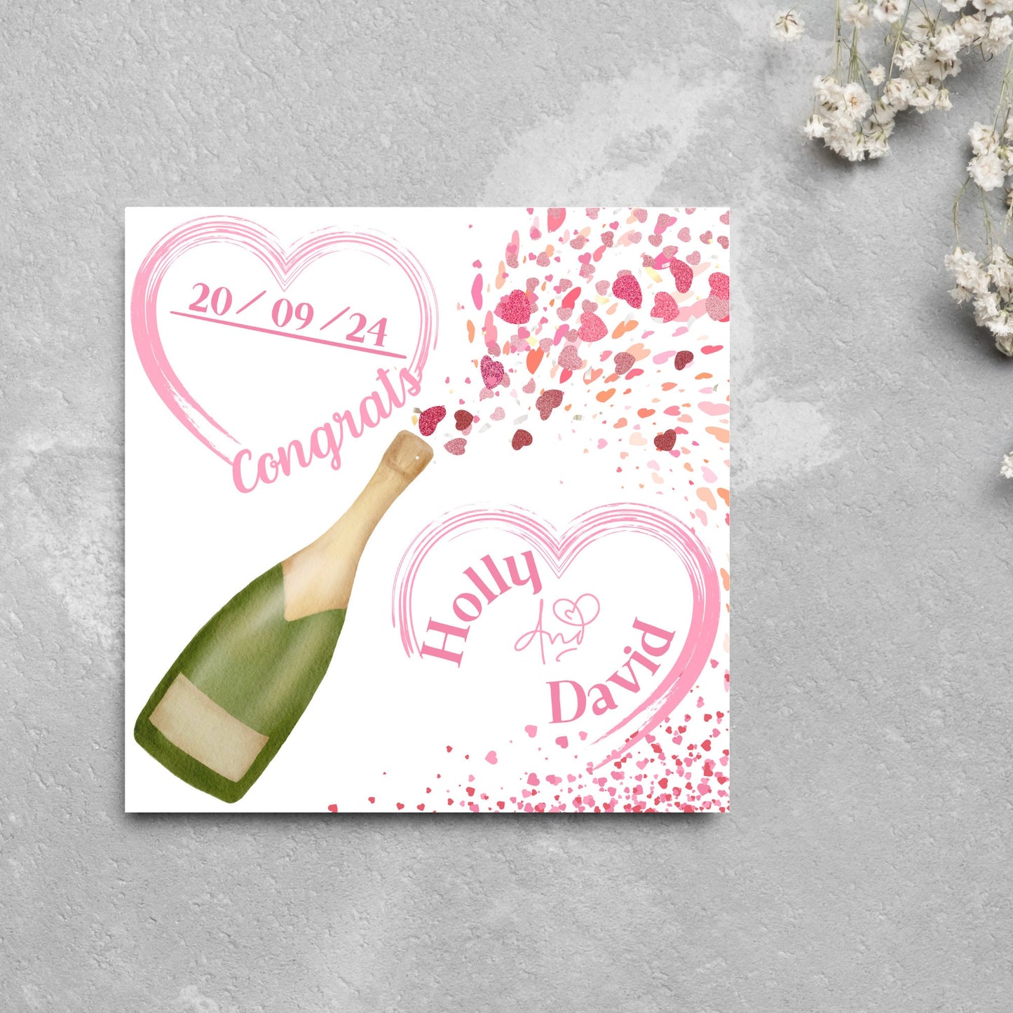 square wedding card with a bottle of champagne bursting with hearts in varying shades of pink. Above the bottle is a heart that holds the date and says contrats, and below is a repeated heart with the names of the couple inside