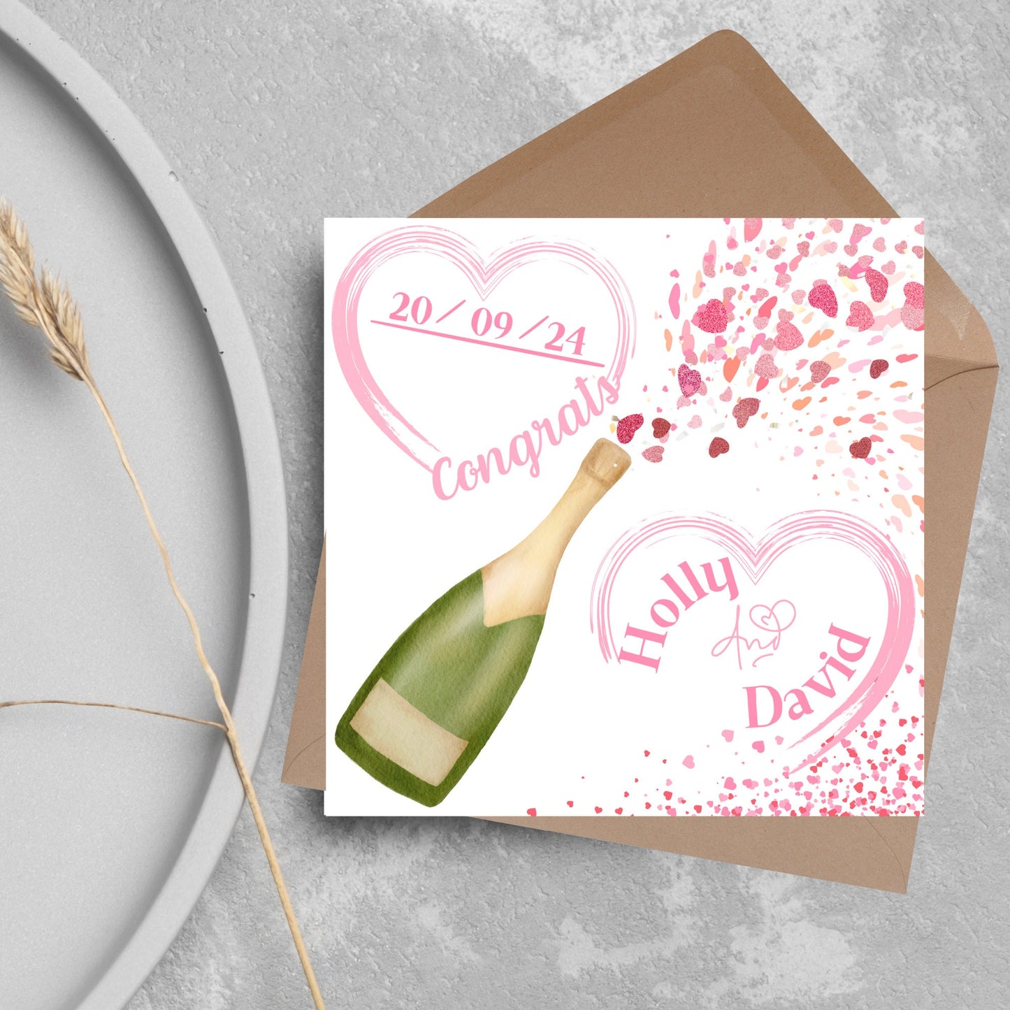 square wedding card with a bottle of champagne bursting with hearts in varying shades of pink. Above the bottle is a heart that holds the date and says contrats, and below is a repeated heart with the names of the couple inside