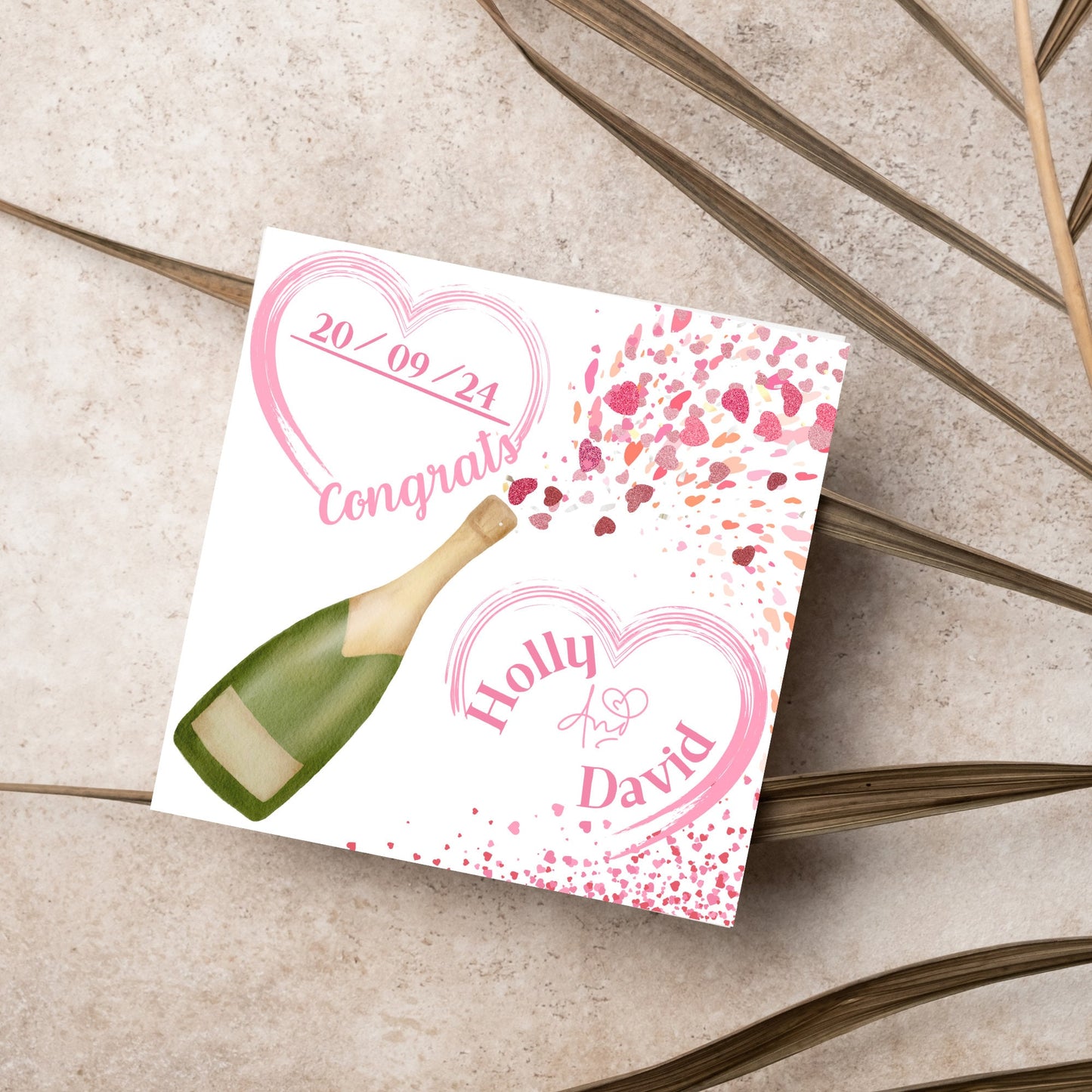 square wedding card with a bottle of champagne bursting with hearts in varying shades of pink. Above the bottle is a heart that holds the date and says contrats, and below is a repeated heart with the names of the couple inside