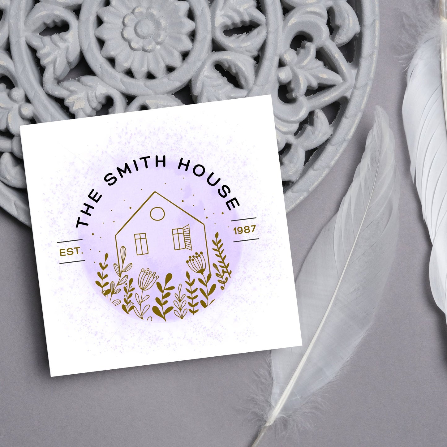 square card with a purple watercolour circle with a line drawing of a house and foliage over it. Arched text reads the smith house on top with est 1987 running through the centre