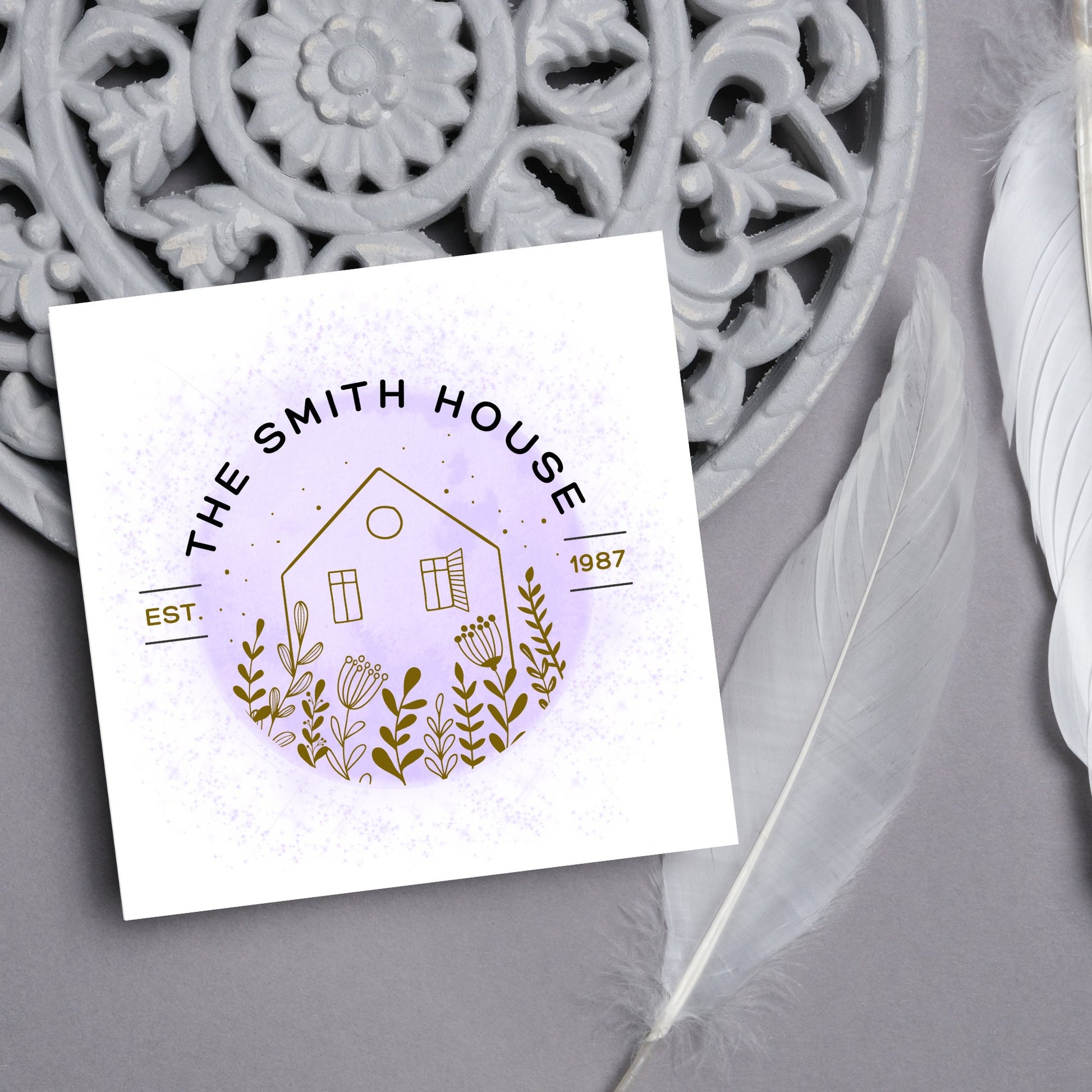 square card with a purple watercolour circle with a line drawing of a house and foliage over it. Arched text reads the smith house on top with est 1987 running through the centre
