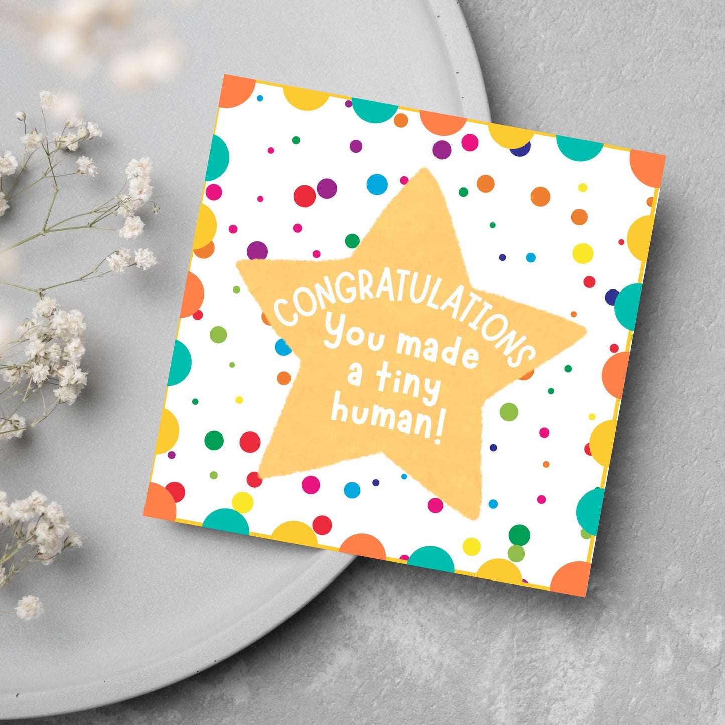 Image of a square card, the card design is a multicoloured polka dot design with a large yellow coloured star in the middle and white text against the star that reads CONGRATULATIONS You made a tiny human!