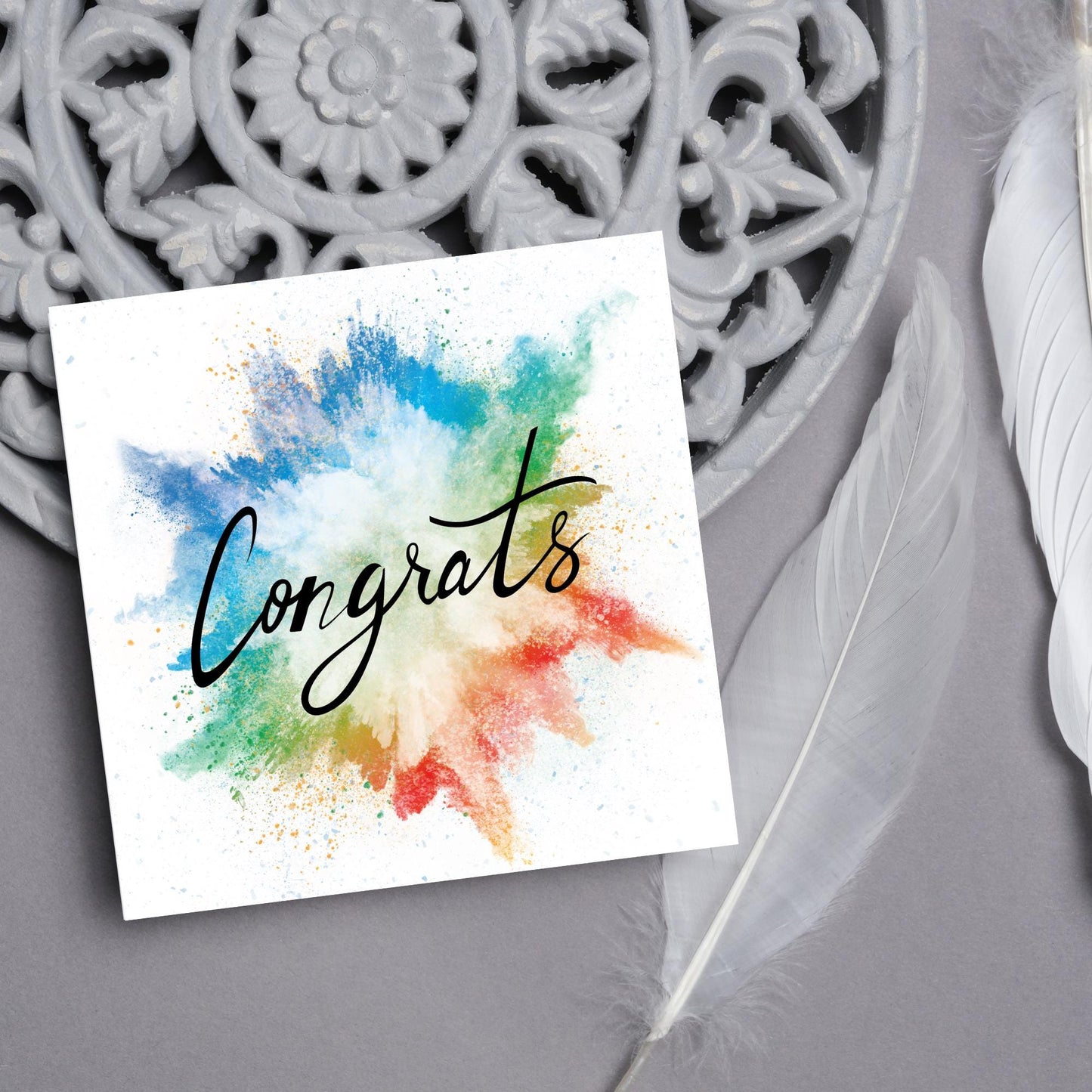 square card with rainbow paint splash against a white background. Black calligraphy style text overlay the paint with congrats