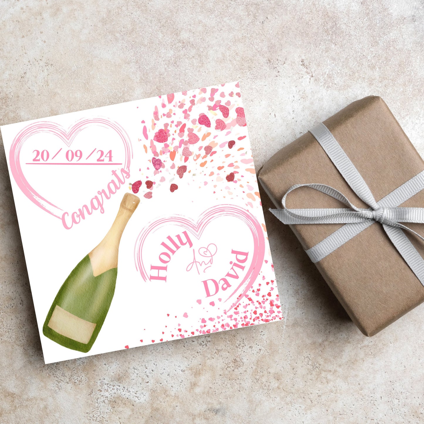 square wedding card with a bottle of champagne bursting with hearts in varying shades of pink. Above the bottle is a heart that holds the date and says contrats, and below is a repeated heart with the names of the couple inside