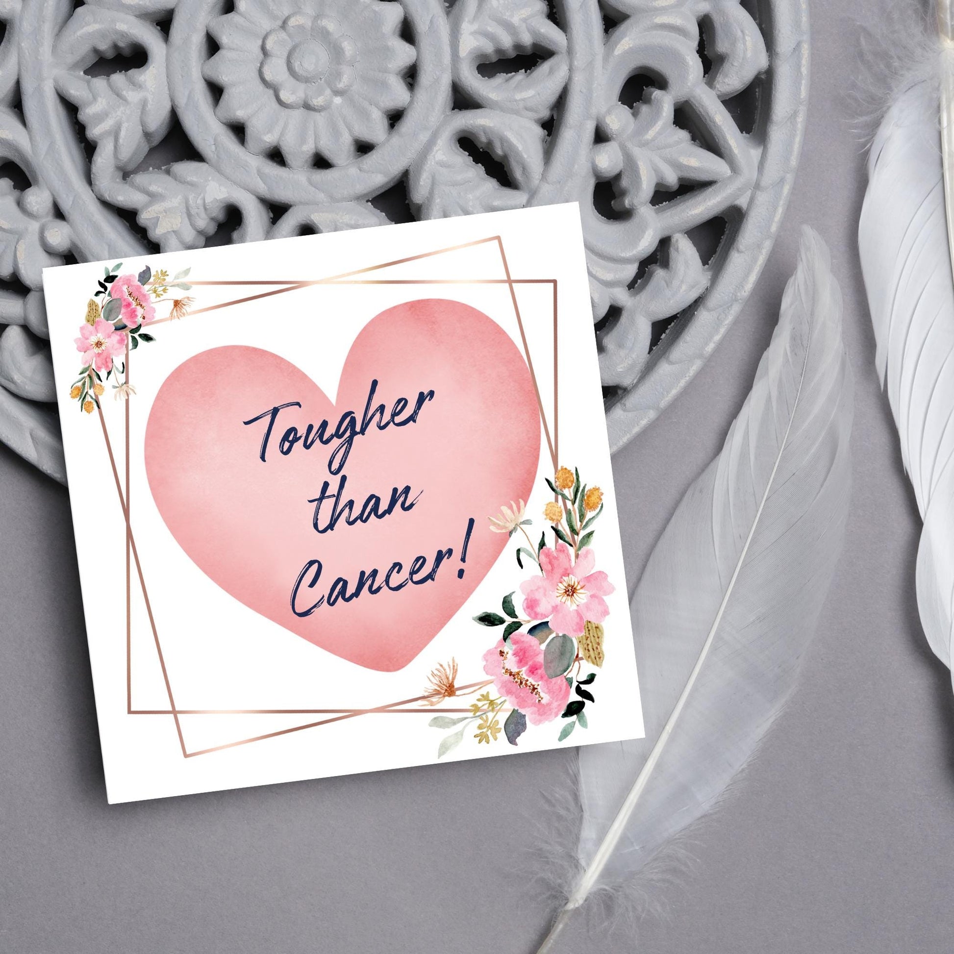 Square white card with a watercolour floral border frame and a pink heart in the centre with the text Tougher than cancer in s handwritten style navy blue font