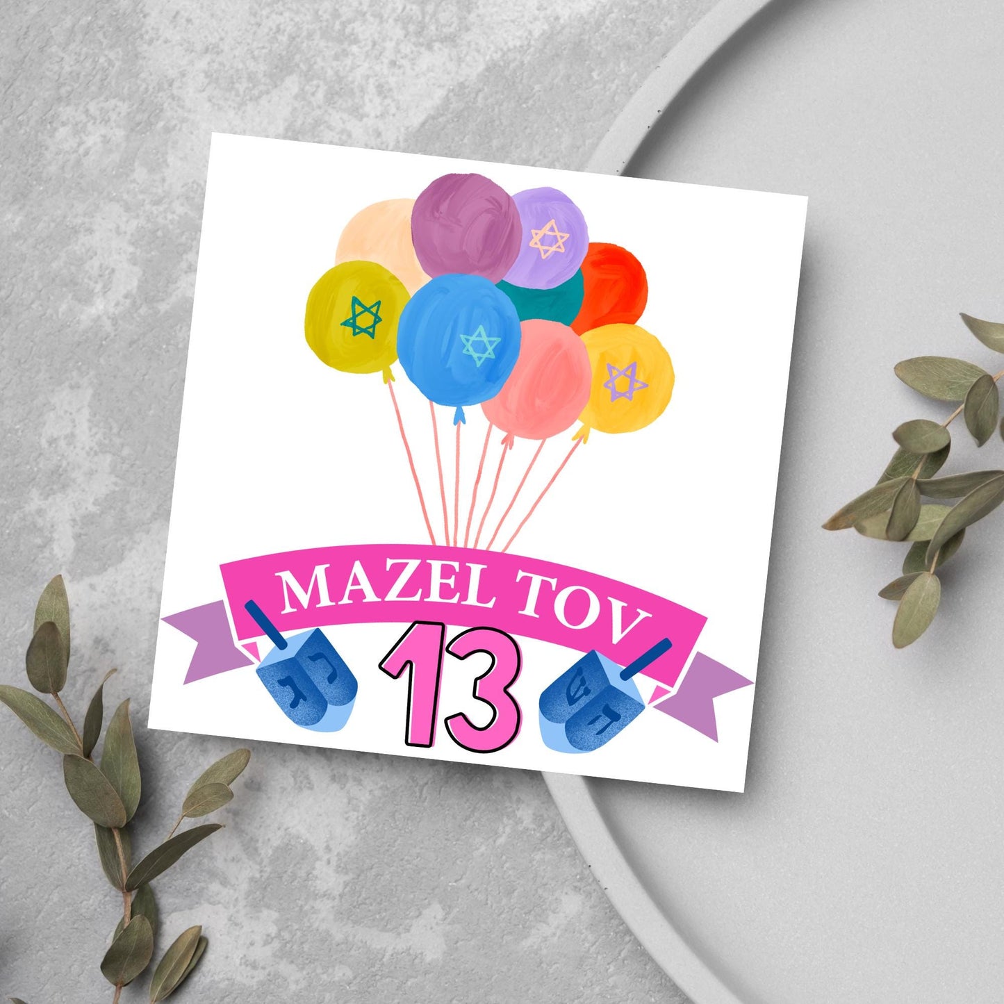square greetings card with a bunch of watercolour design balloons decorated with stars of david. Below is a pink banner which reads mazel tov and the number 13 between a dreidel toy