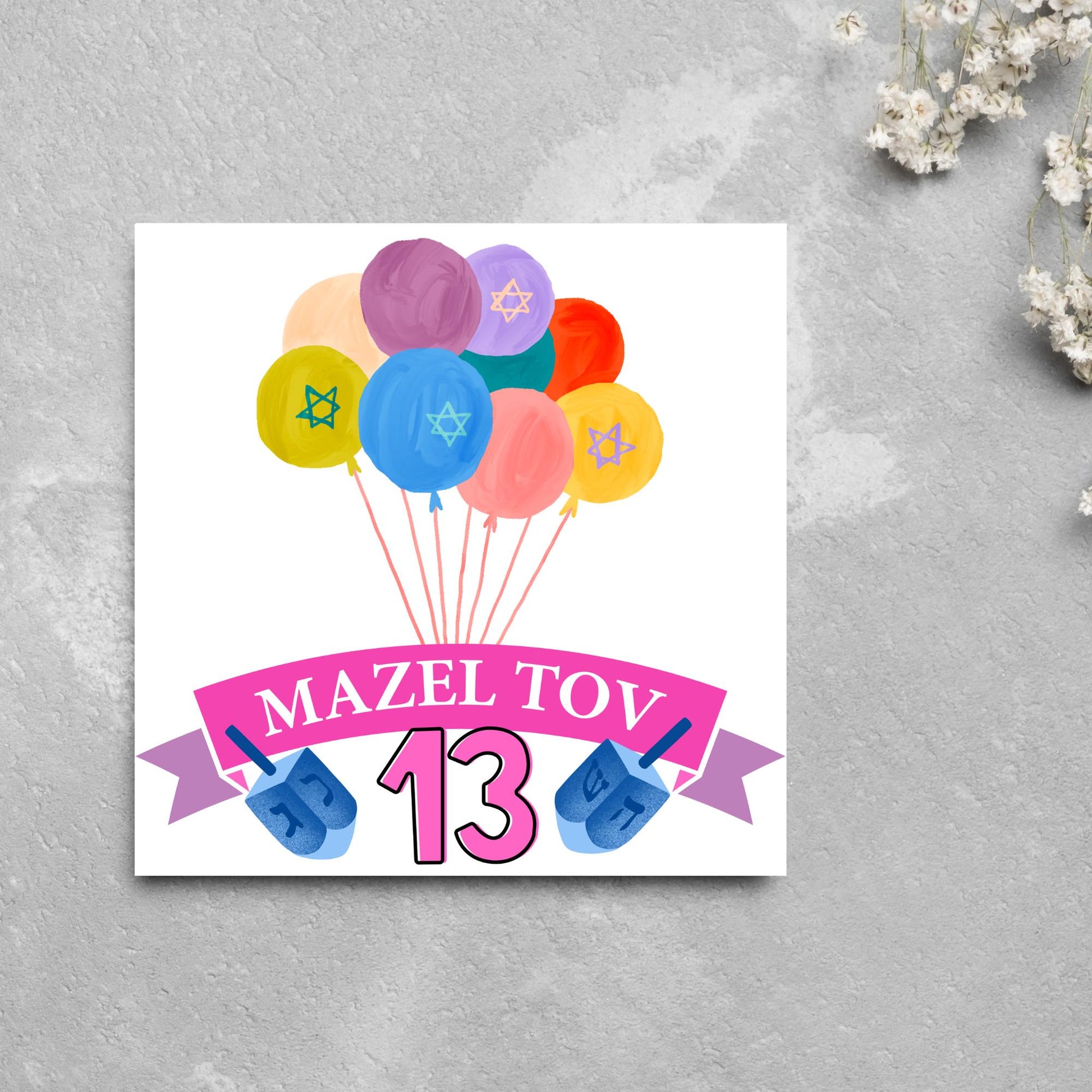 square greetings card with a bunch of watercolour design balloons decorated with stars of david. Below is a pink banner which reads mazel tov and the number 13 between a dreidel toy