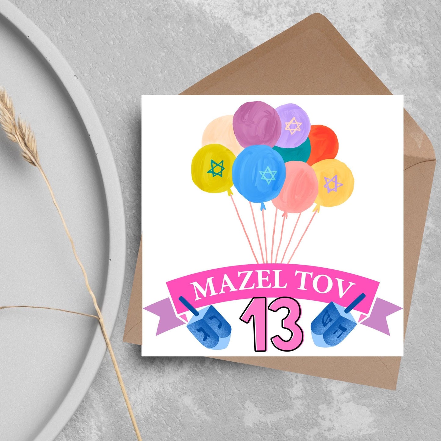 square greetings card with a bunch of watercolour design balloons decorated with stars of david. Below is a pink banner which reads mazel tov and the number 13 between a dreidel toy