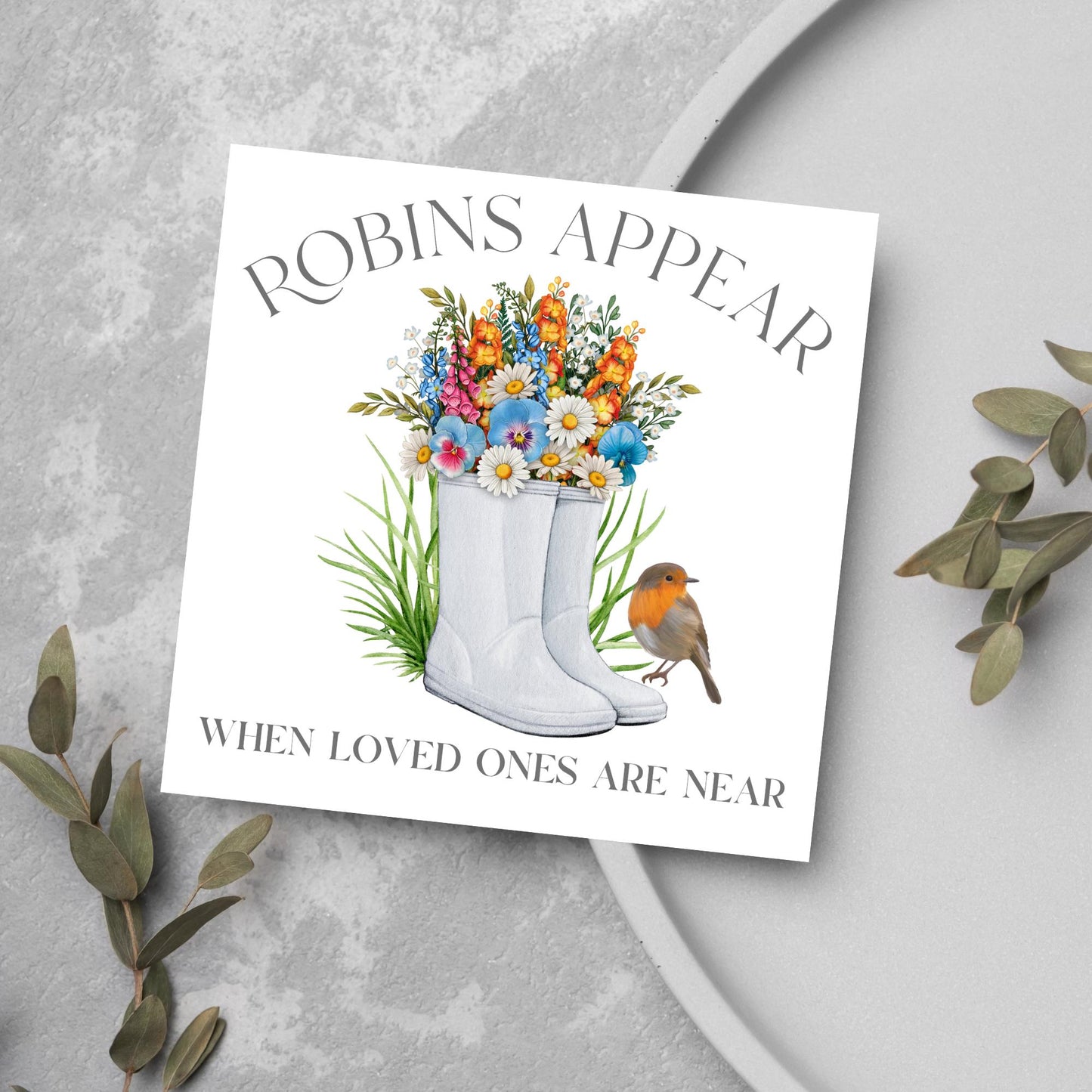 Square card with a watercolour image of a robin sitting on a pair of wellington boots that at filled with flowers. Elegant text reads Robins Appear when loved ones are near