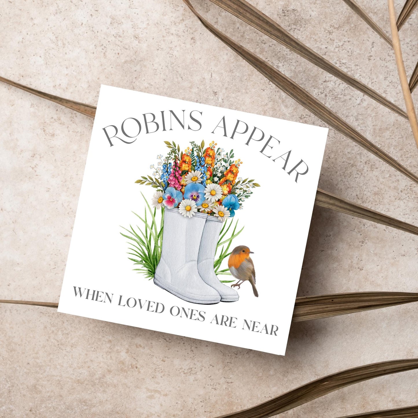Square card with a watercolour image of a robin sitting on a pair of wellington boots that at filled with flowers. Elegant text reads Robins Appear when loved ones are near