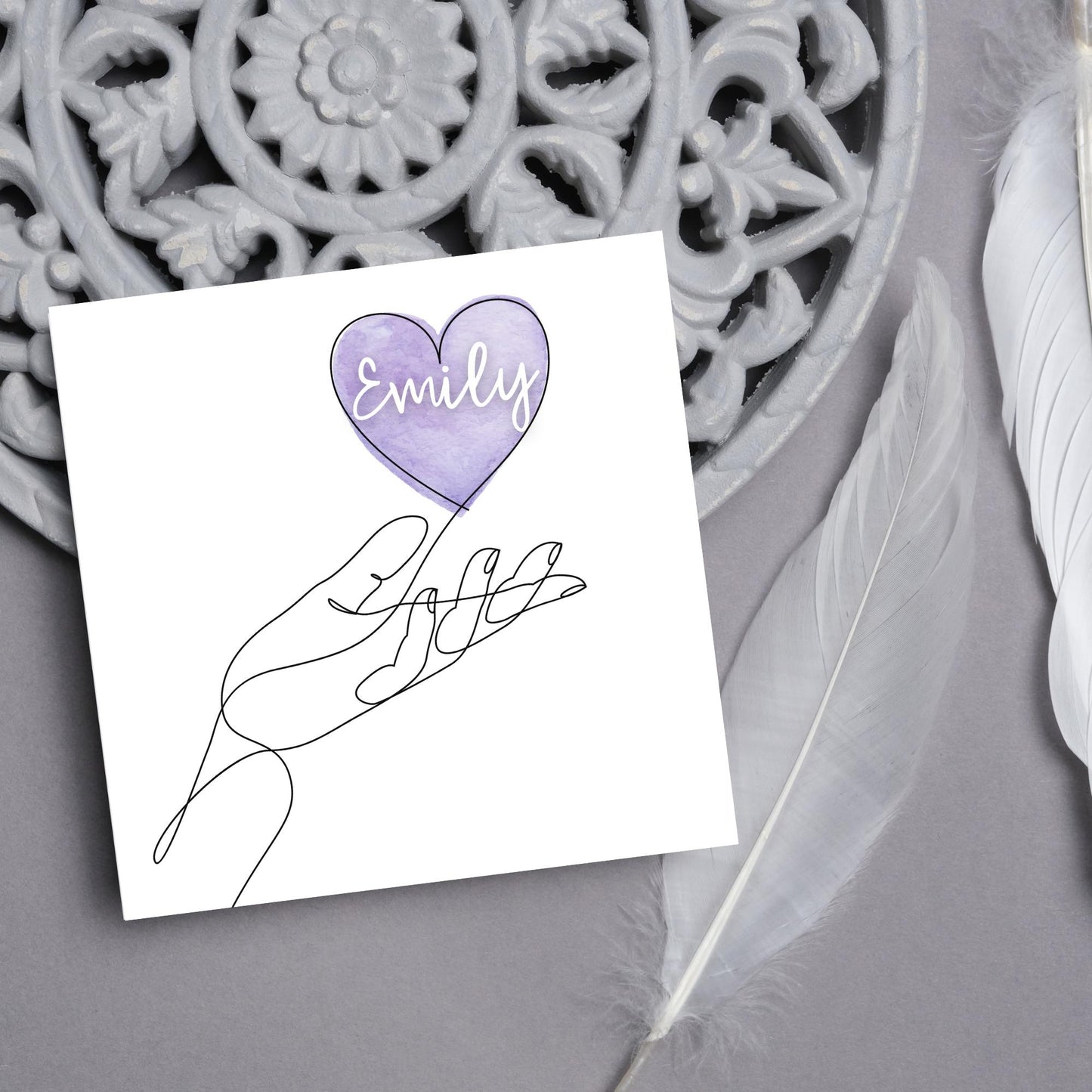 square card with a simple black and white one line drawing of an open hand with a heart rising from the hand. the heart has a purple background and has a personalised name written in a white cursive text