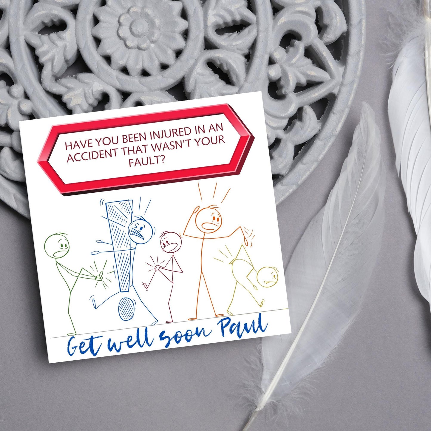 Square Get well soon card with a red sign which says have you been injured in an accident that wasn't your fault? above stick person cartoons of various injuries. Underneath is a handwritten style message that reads get well soon paul