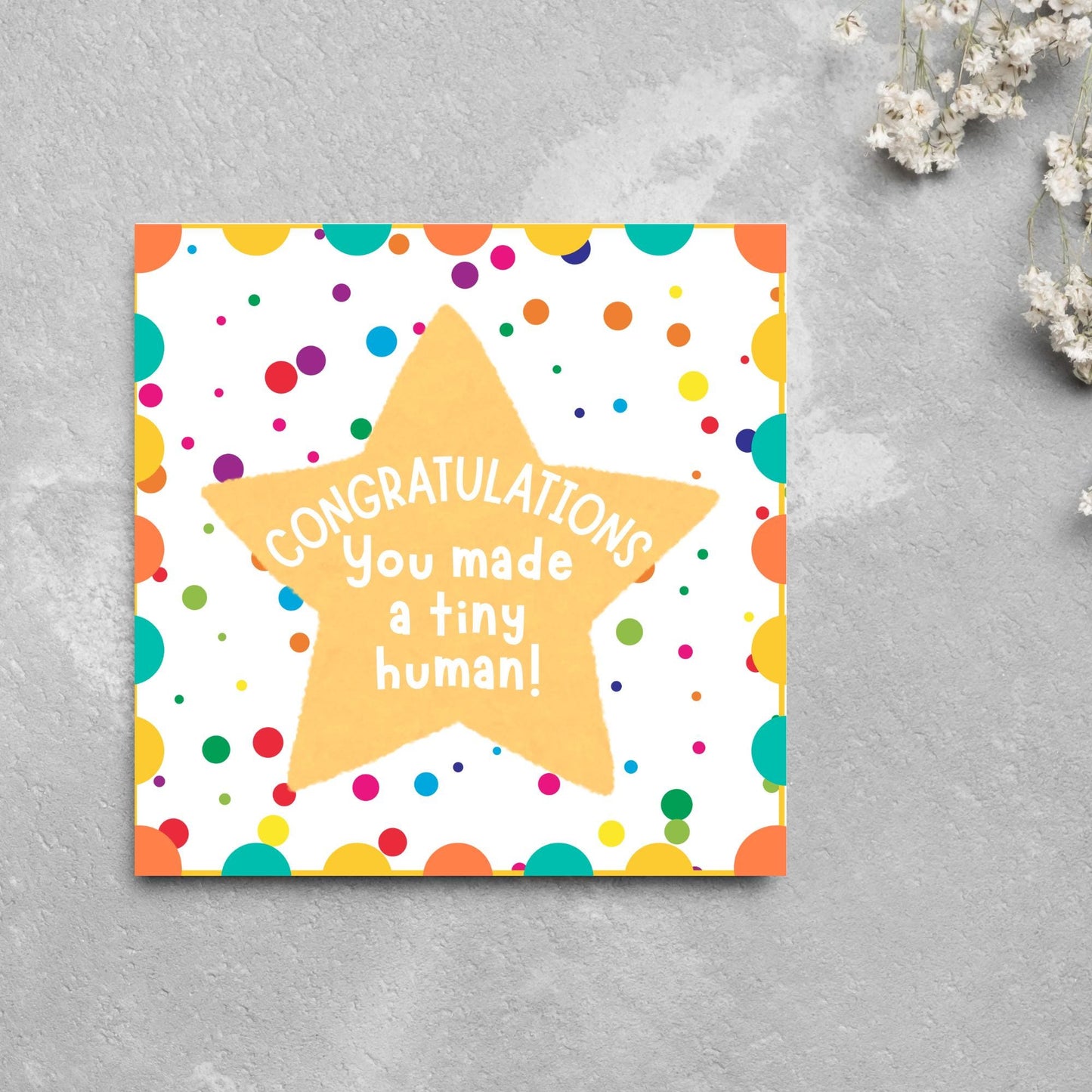 Image of a square card, the card design is a multicoloured polka dot design with a large yellow coloured star in the middle and white text against the star that reads CONGRATULATIONS You made a tiny human!