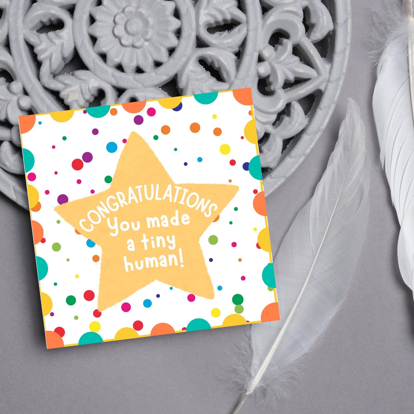 Image of a square card, the card design is a multicoloured polka dot design with a large yellow coloured star in the middle and white text against the star that reads CONGRATULATIONS You made a tiny human!