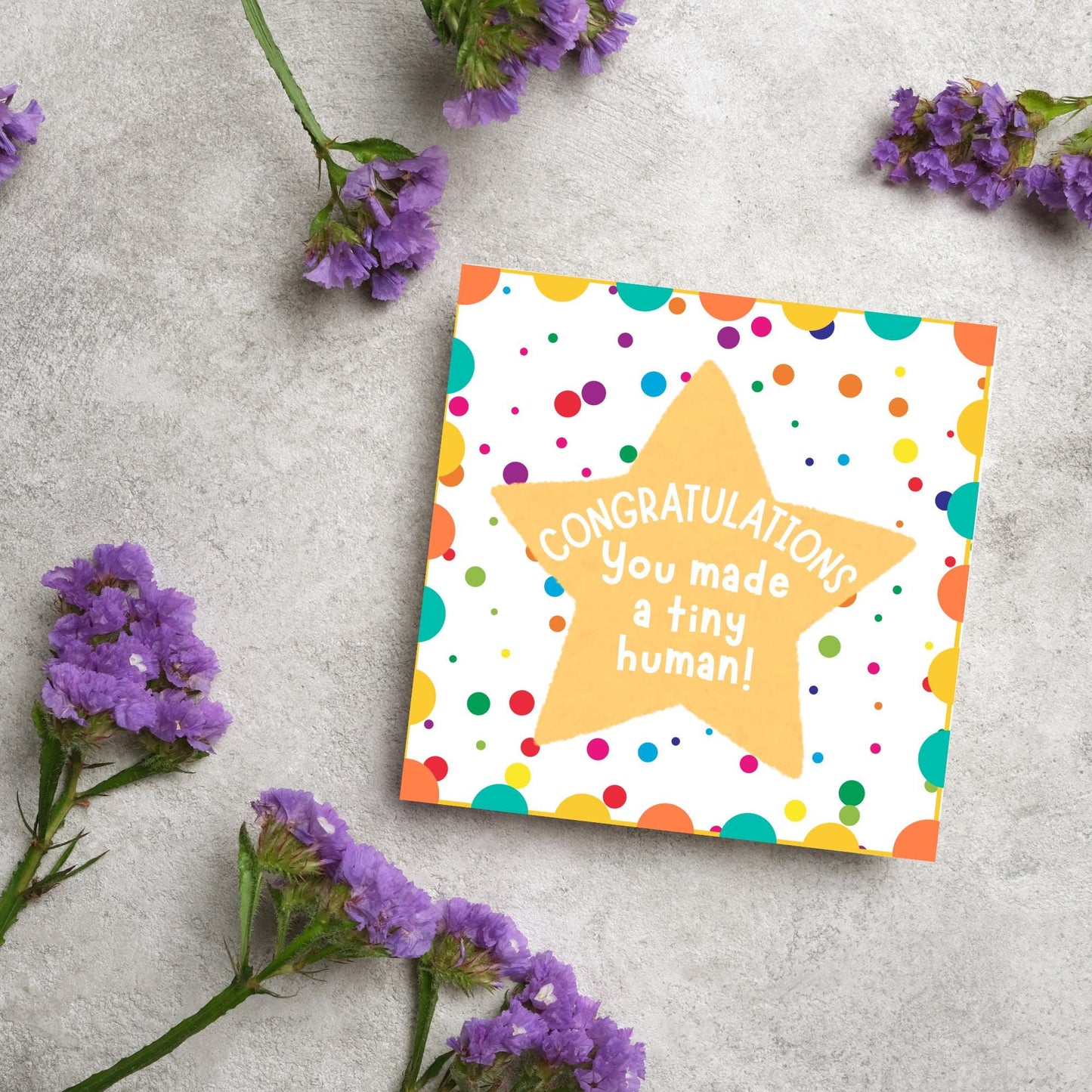 Image of a square card, the card design is a multicoloured polka dot design with a large yellow coloured star in the middle and white text against the star that reads CONGRATULATIONS You made a tiny human!