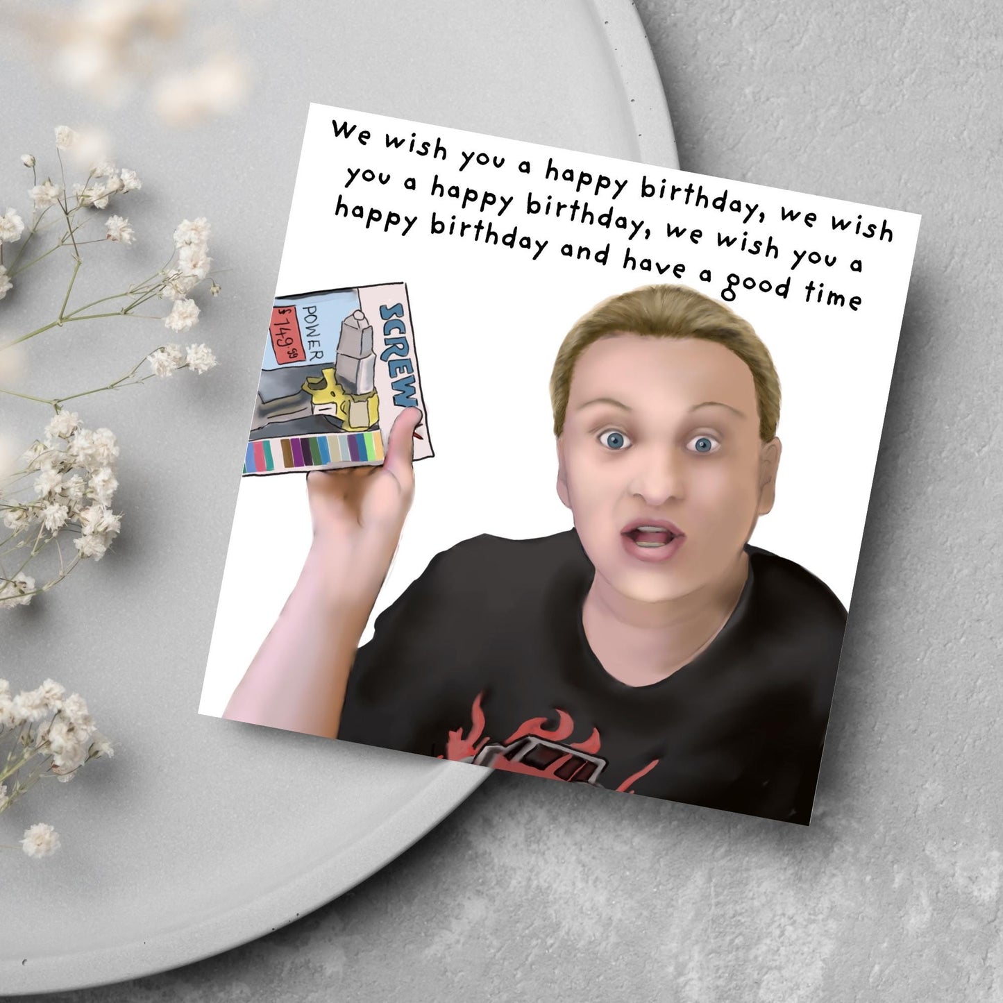 Square birthday card with a hand drawn image of Kerry from this country looking shocked and holding up a screwfix catalogue with the text we wish you a happy birthday, we wish you a happy birthday, we wish you a happy birthday and have a good time