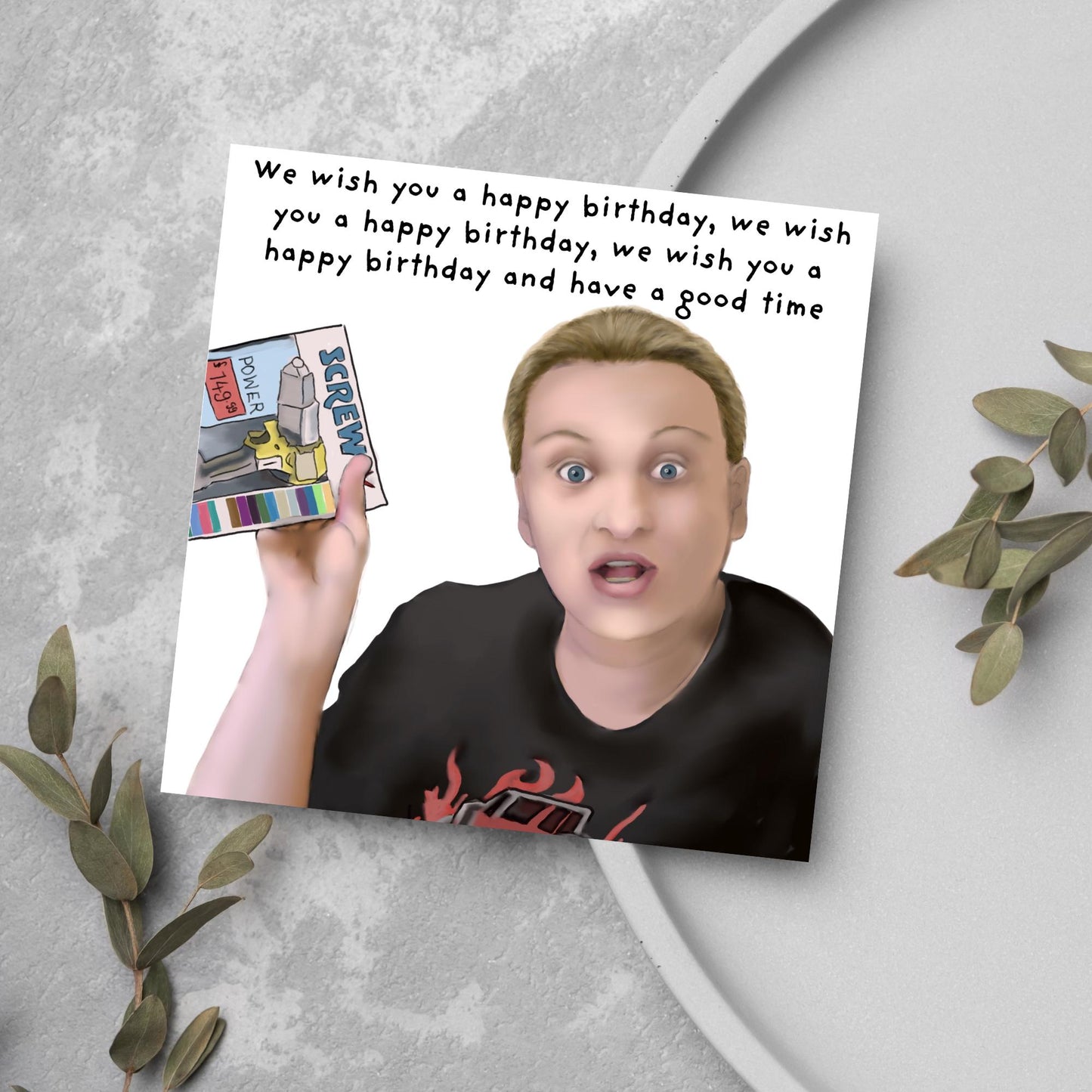 Square birthday card with a hand drawn image of Kerry from this country looking shocked and holding up a screwfix catalogue with the text we wish you a happy birthday, we wish you a happy birthday, we wish you a happy birthday and have a good time