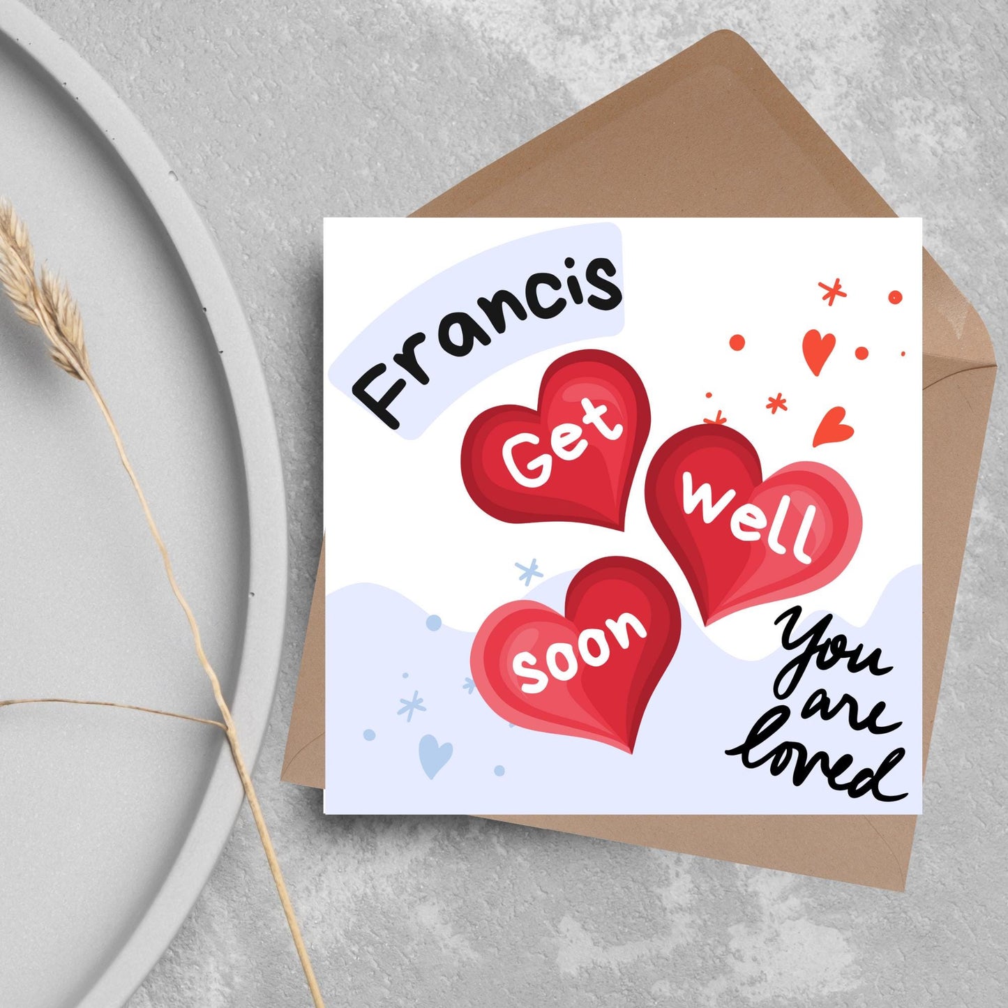 square card with white and blue background. 3 red hearts are in the centre of the card with get well soon overlayed in white, the top corner has curved text with the recipients name and in the bottom corner the text you are loved in black cursive