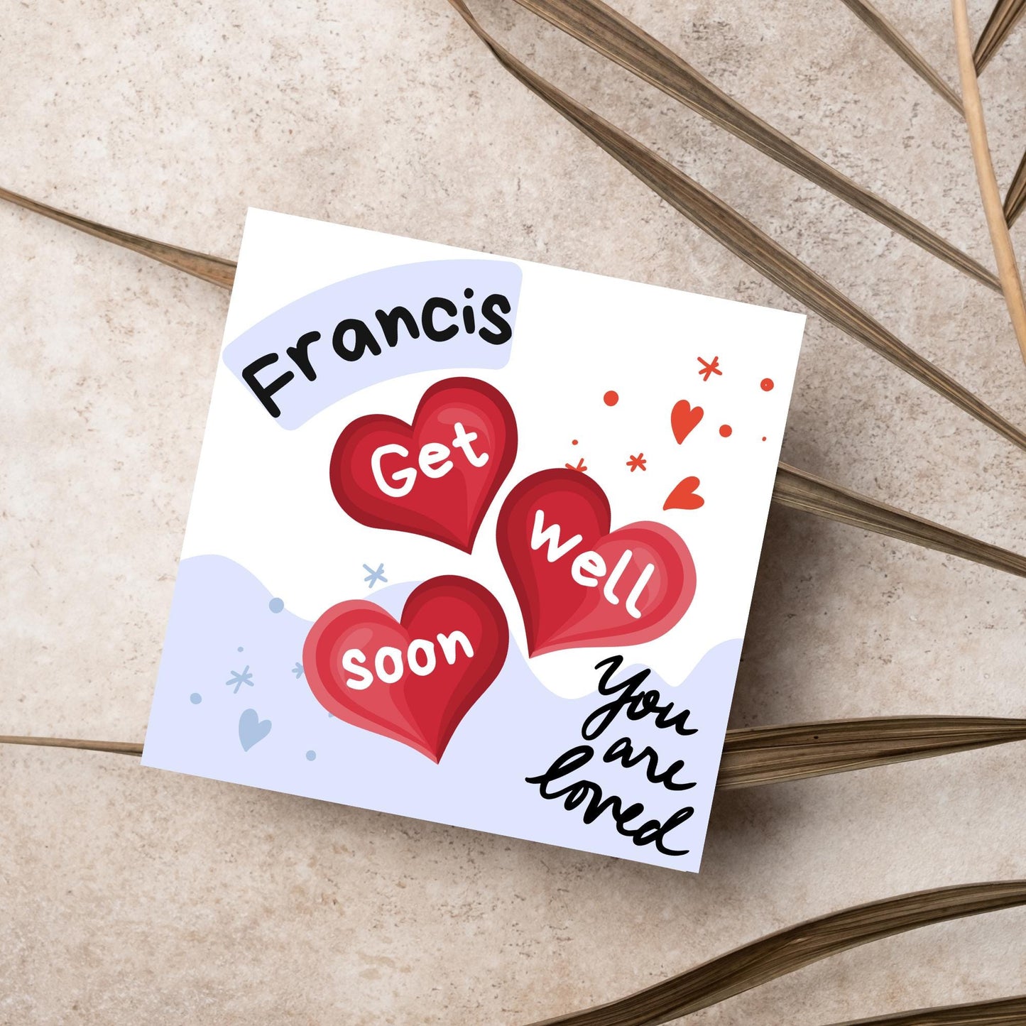 square card with white and blue background. 3 red hearts are in the centre of the card with get well soon overlayed in white, the top corner has curved text with the recipients name and in the bottom corner the text you are loved in black cursive