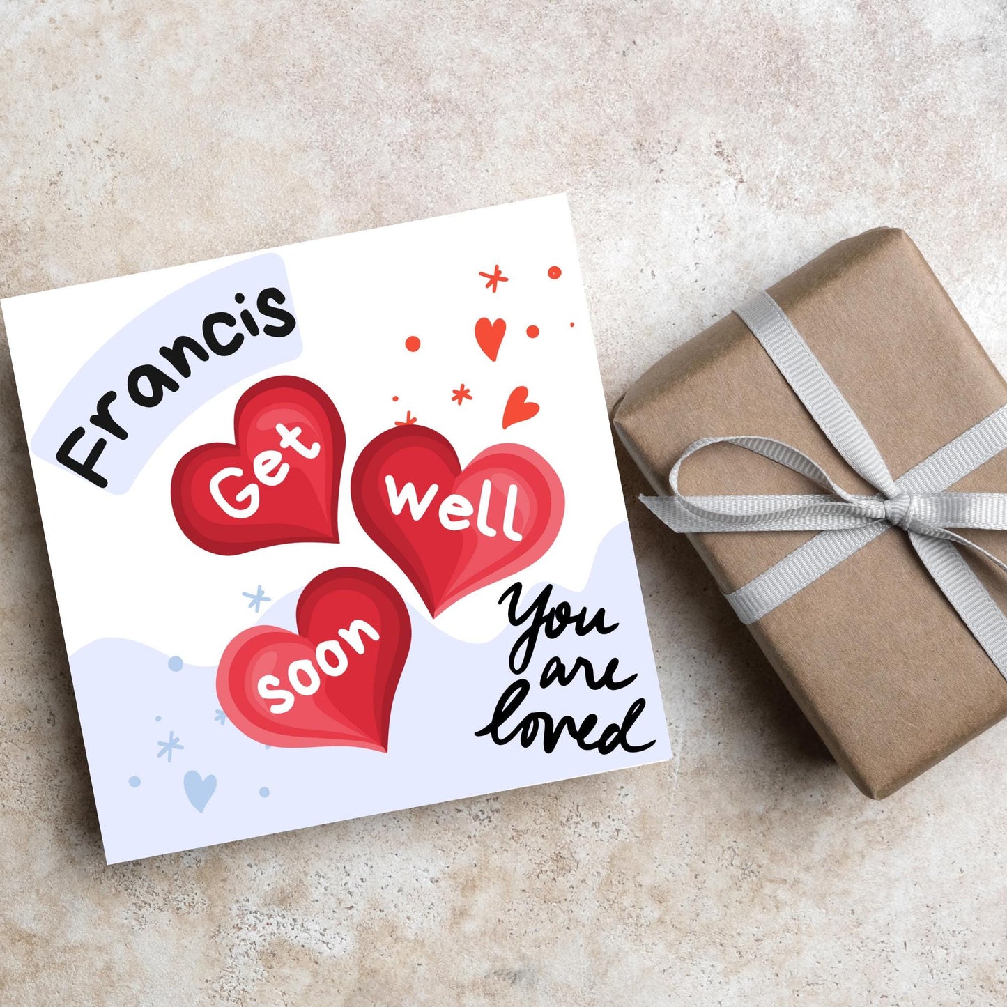 square card with white and blue background. 3 red hearts are in the centre of the card with get well soon overlayed in white, the top corner has curved text with the recipients name and in the bottom corner the text you are loved in black cursive