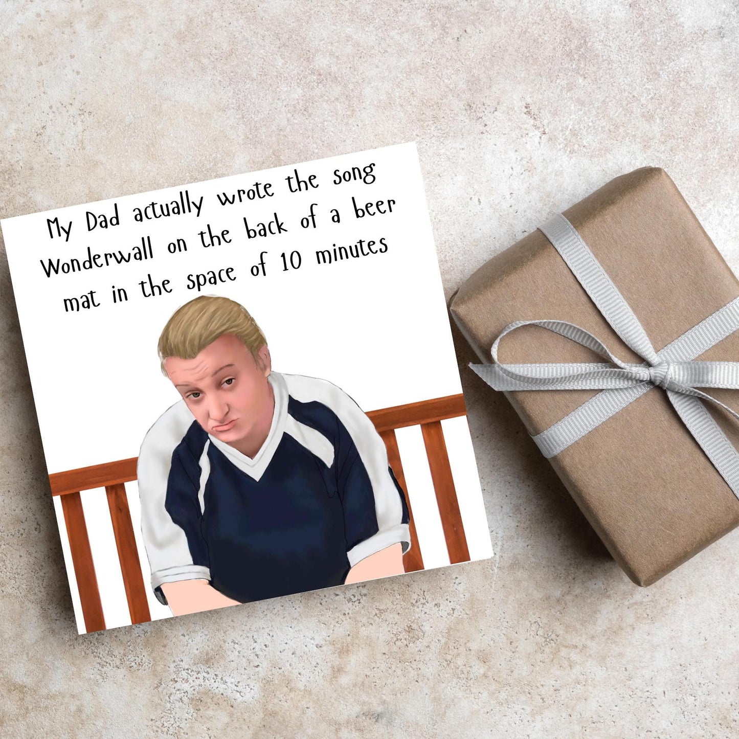 square card with a hand drawn image of kerry from this country sitting on a bench with handwritten style text above - My Dad actually wrote the song Wonderwall on the back of a beer mat in the space of 10 minutes