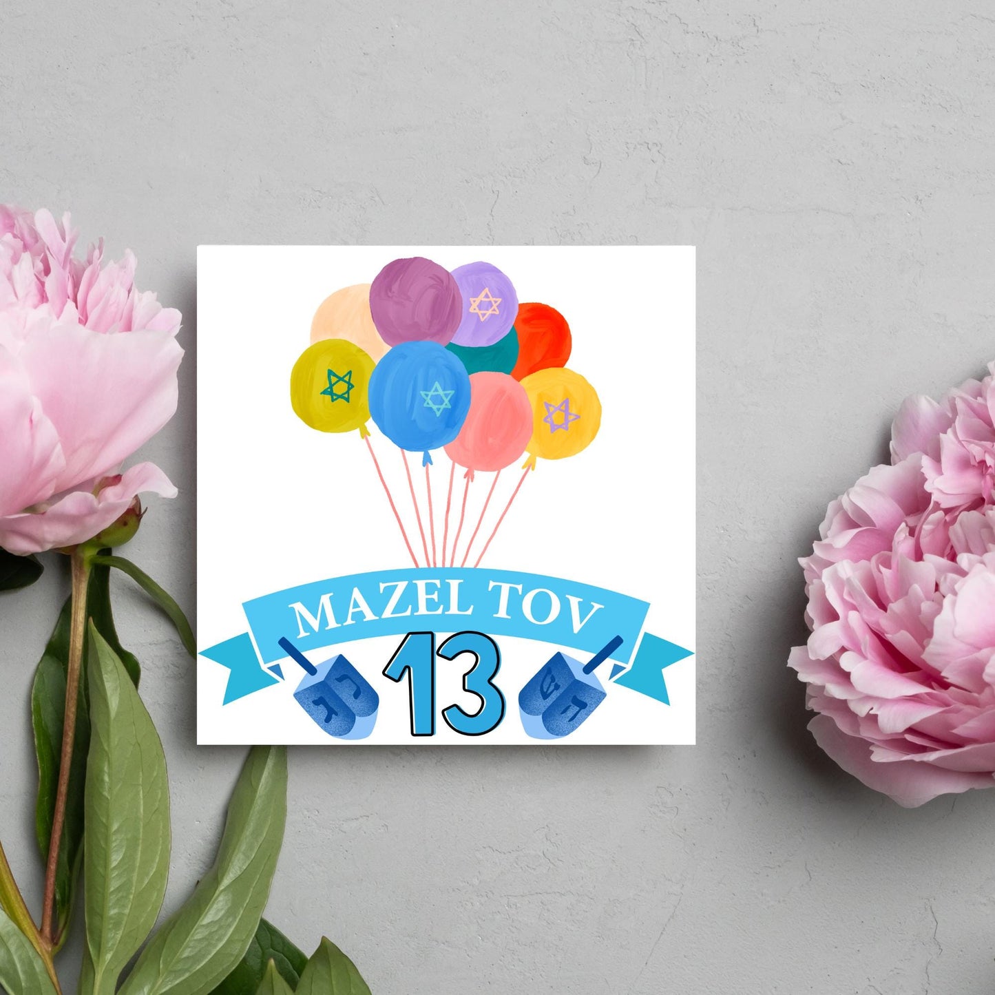 square greetings card with a bunch of watercolour design balloons decorated with stars of david. Below is a blue banner which reads mazel tov and the number 13 between a dreidel toy