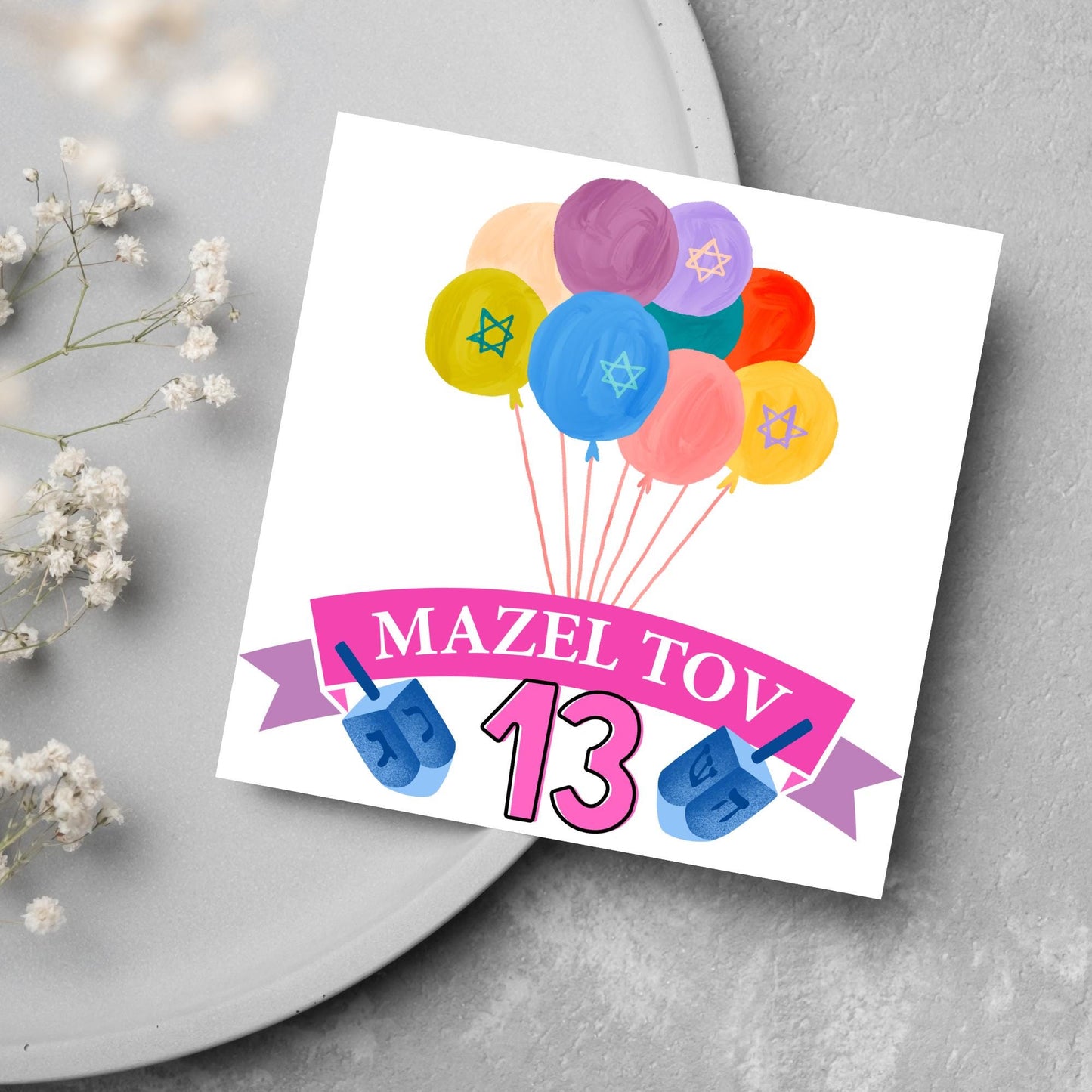 square greetings card with a bunch of watercolour design balloons decorated with stars of david. Below is a pink banner which reads mazel tov and the number 13 between a dreidel toy