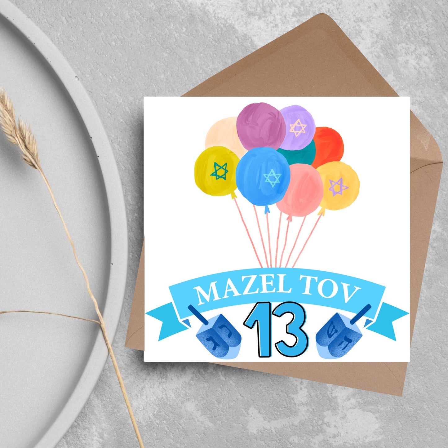 square greetings card with a bunch of watercolour design balloons decorated with stars of david. Below is a blue banner which reads mazel tov and the number 13 between a dreidel toy