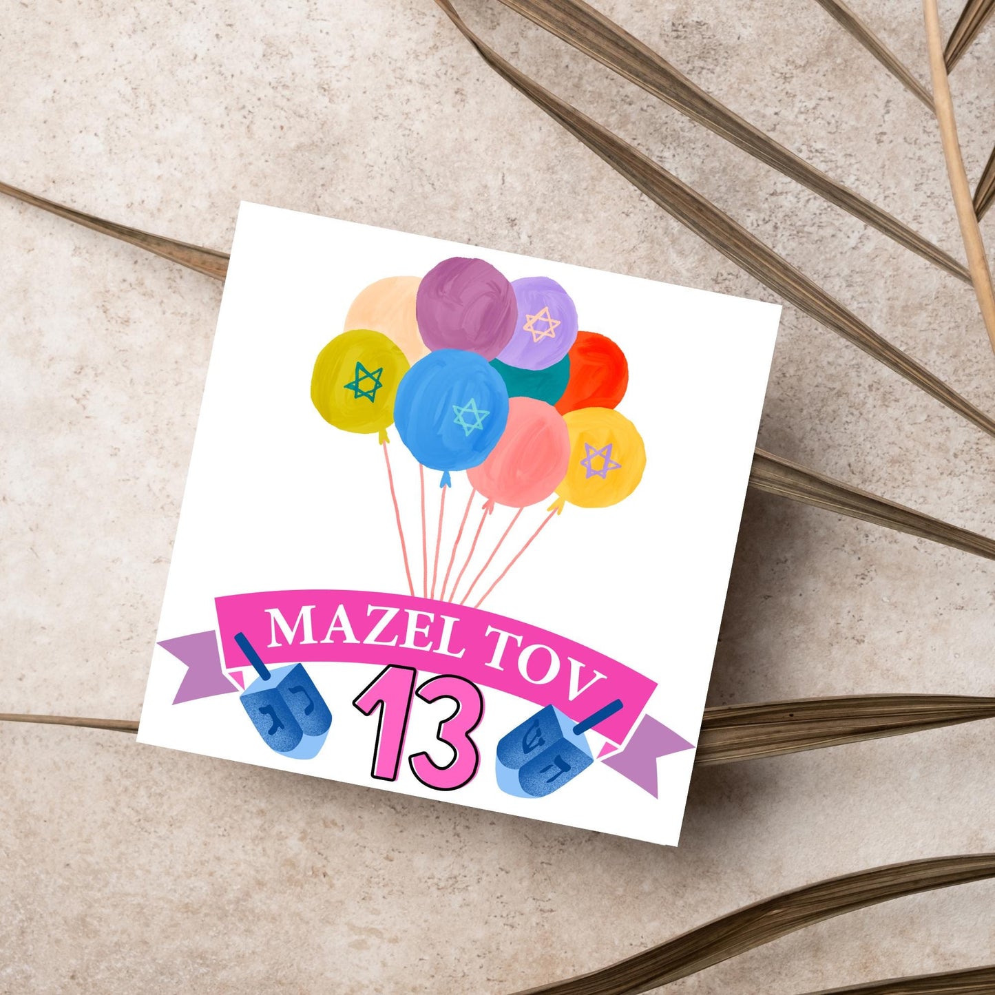 square greetings card with a bunch of watercolour design balloons decorated with stars of david. Below is a pink banner which reads mazel tov and the number 13 between a dreidel toy