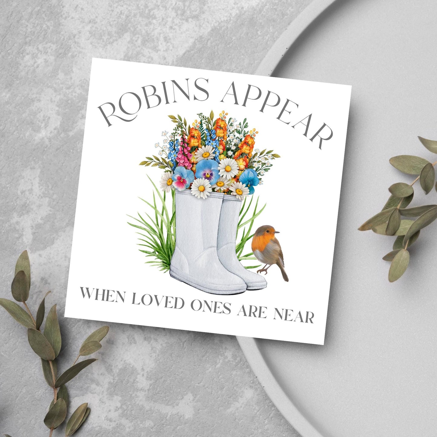 Square card with a watercolour image of a robin sitting on a pair of wellington boots that at filled with flowers. Elegant text reads Robins Appear when loved ones are near