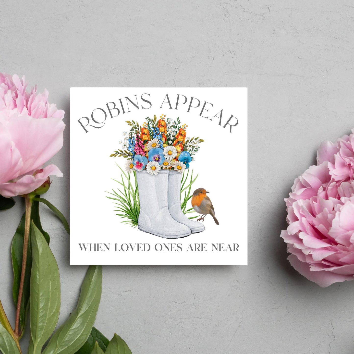 Square card with a watercolour image of a robin sitting on a pair of wellington boots that at filled with flowers. Elegant text reads Robins Appear when loved ones are near