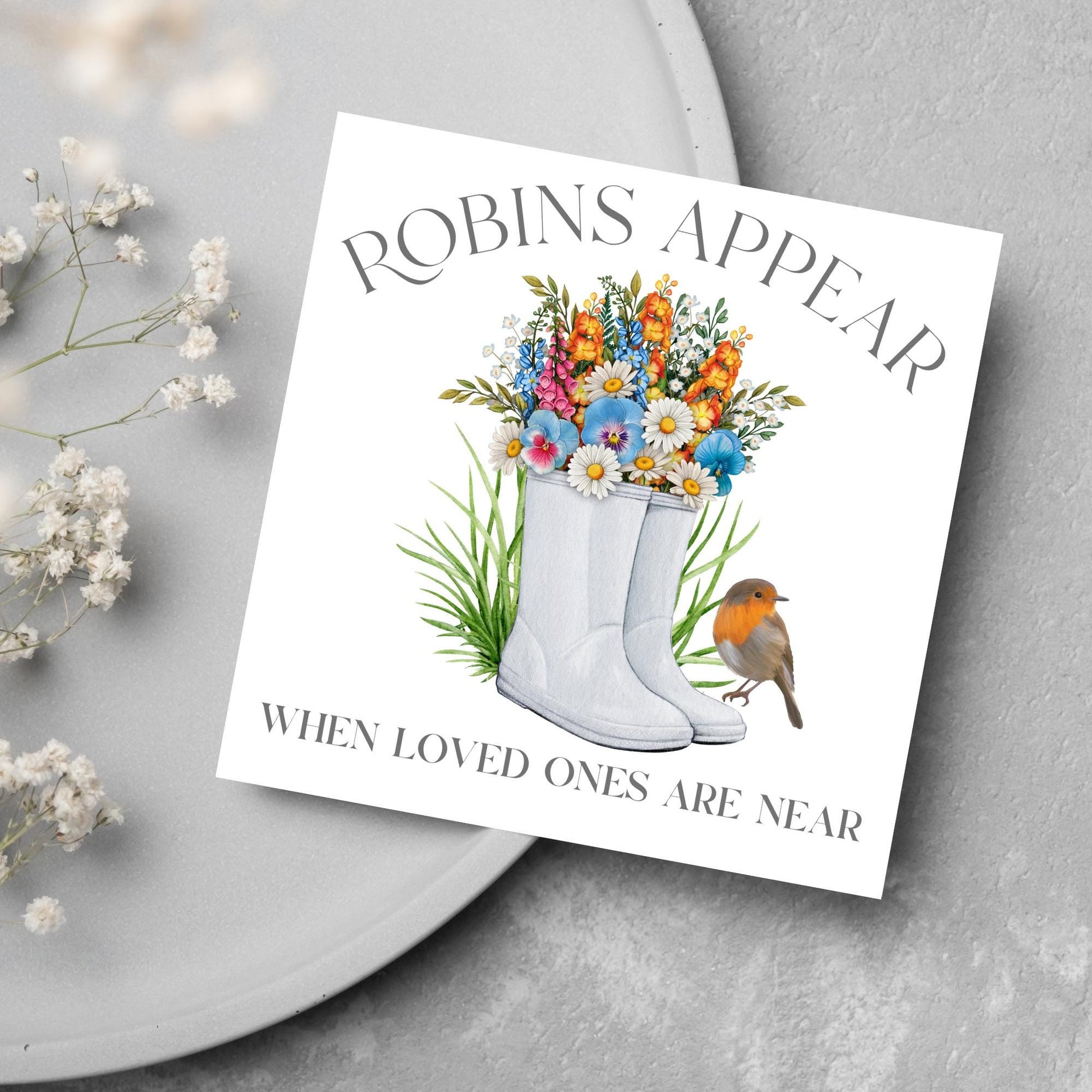 Square card with a watercolour image of a robin sitting on a pair of wellington boots that at filled with flowers. Elegant text reads Robins Appear when loved ones are near