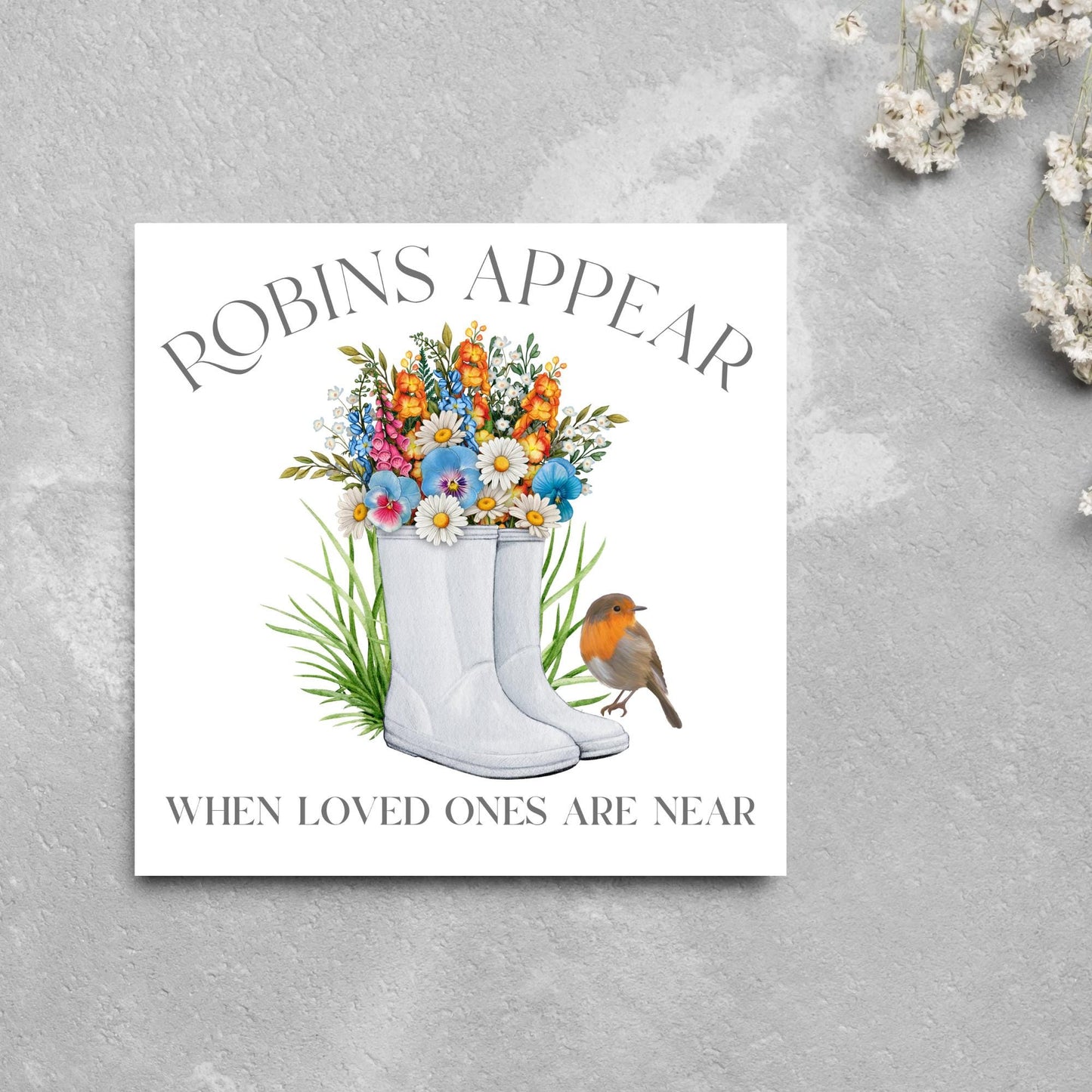 Square card with a watercolour image of a robin sitting on a pair of wellington boots that at filled with flowers. Elegant text reads Robins Appear when loved ones are near