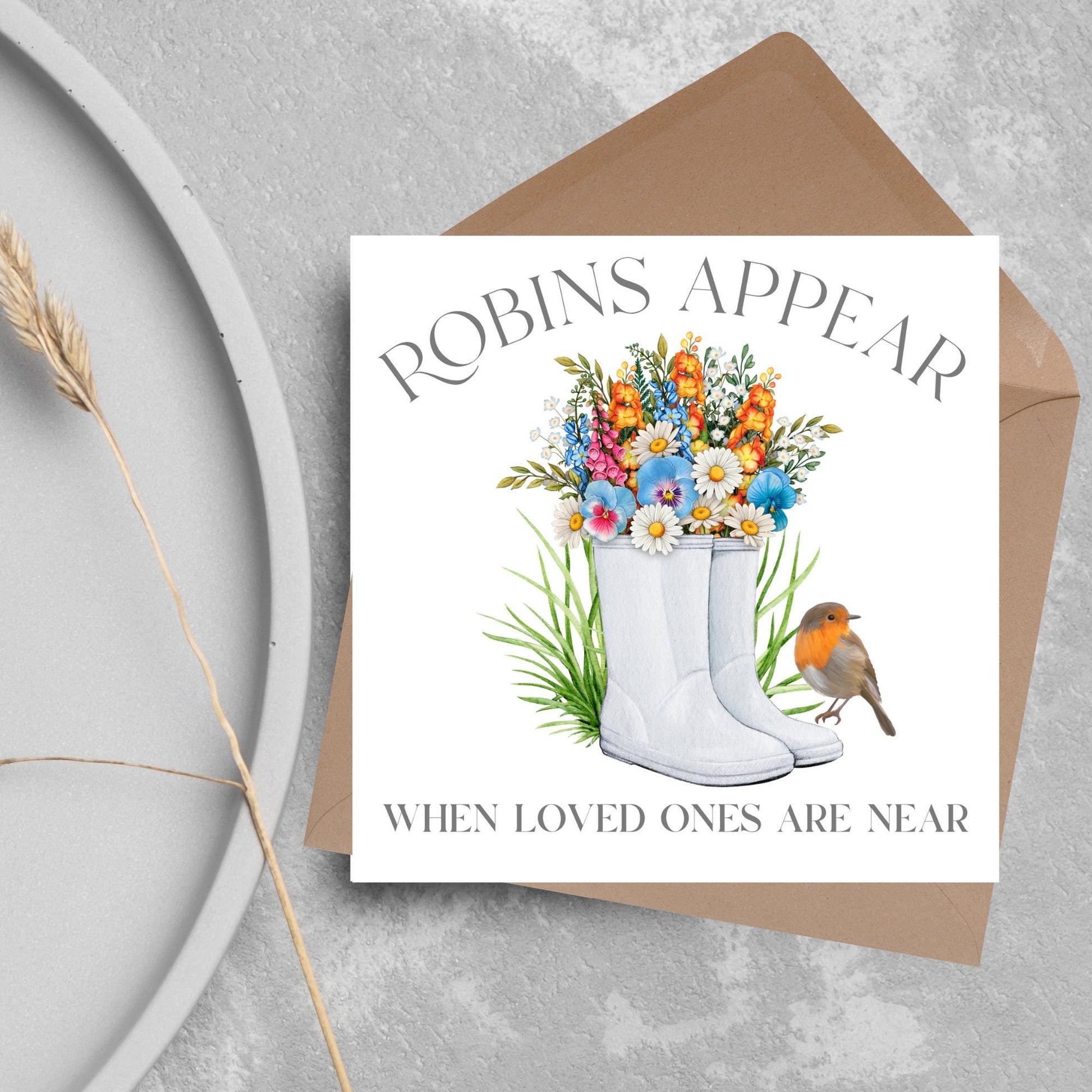 Square card with a watercolour image of a robin sitting on a pair of wellington boots that at filled with flowers. Elegant text reads Robins Appear when loved ones are near