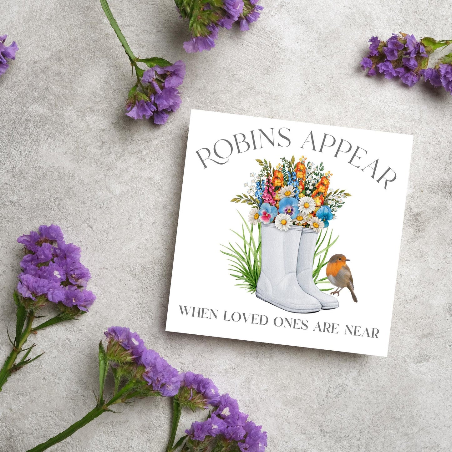 Square card with a watercolour image of a robin sitting on a pair of wellington boots that at filled with flowers. Elegant text reads Robins Appear when loved ones are near